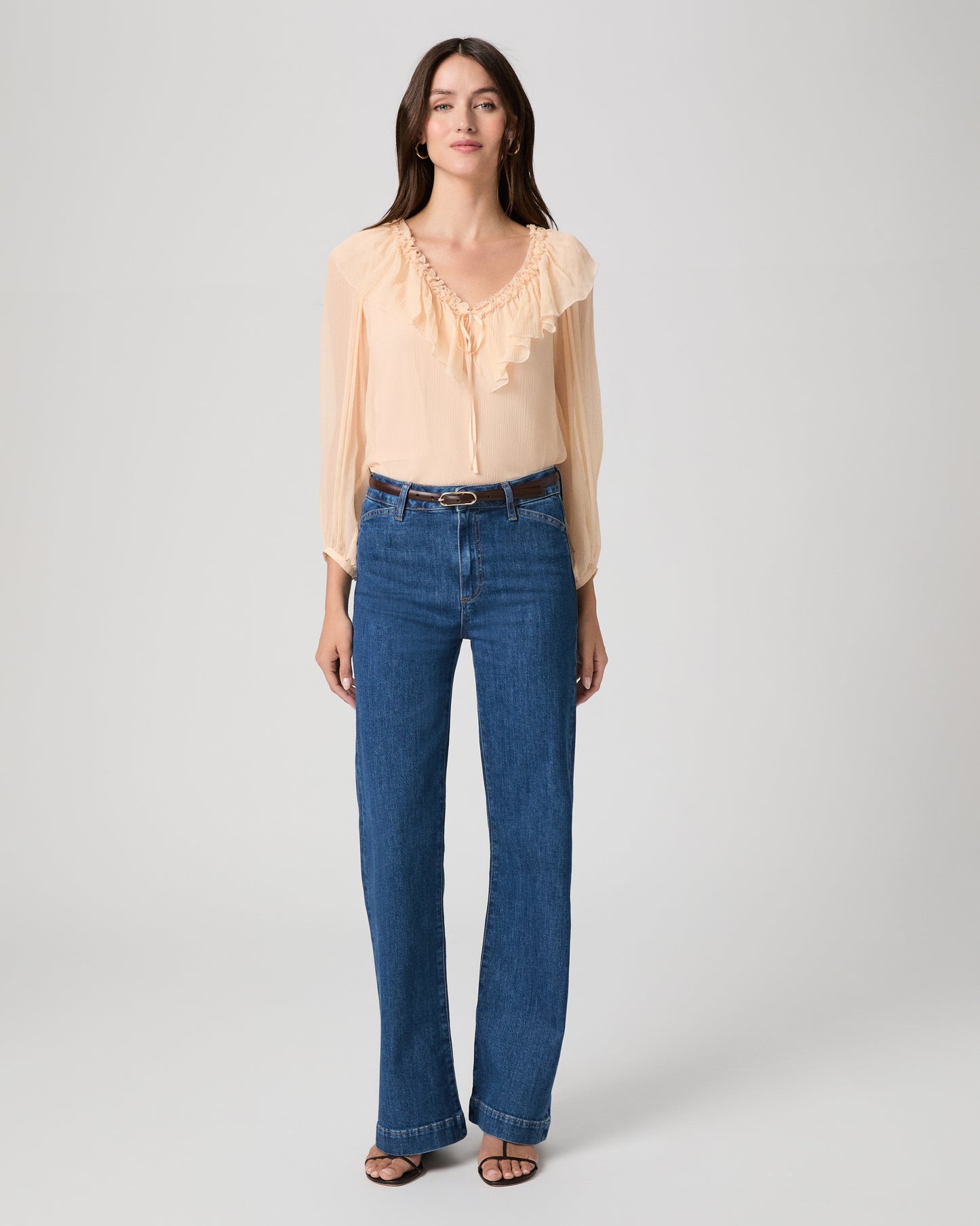 Women wearing light peach color blouse paired with medium wash denim against a white background