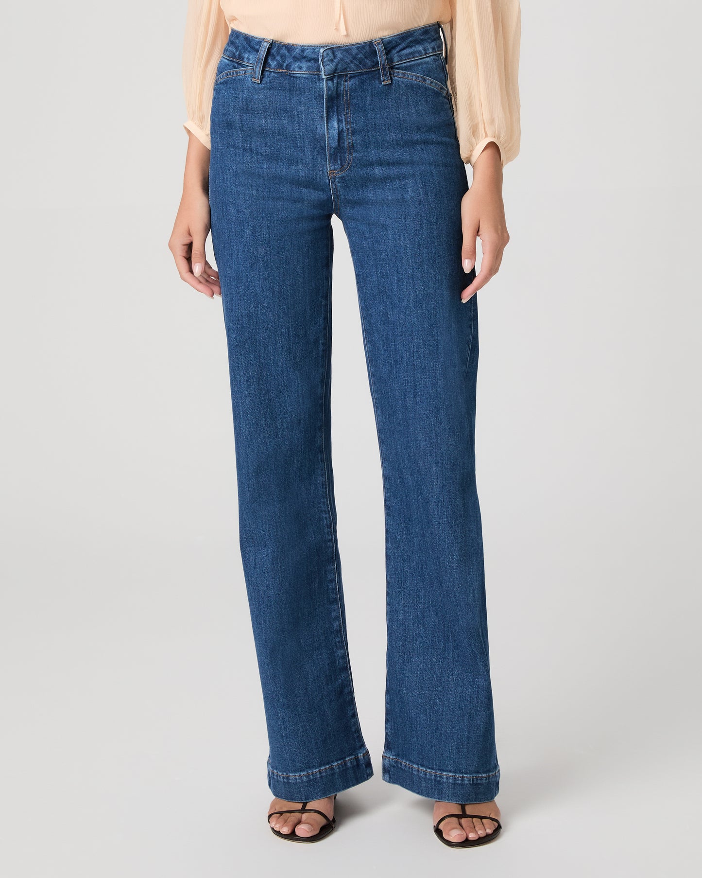 Women wearing light peach color blouse paired with medium wash denim against a white background