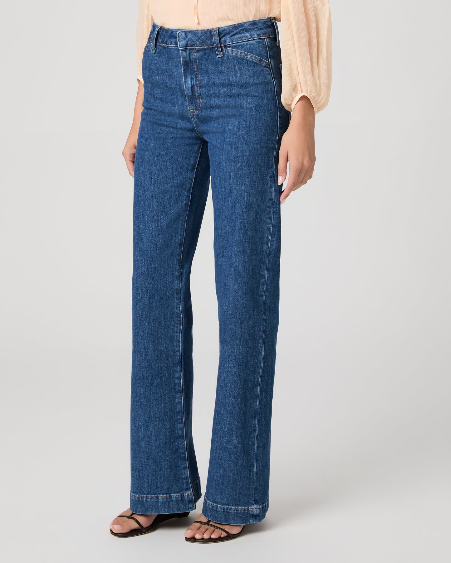 Women wearing light peach color blouse paired with medium wash denim against a white background