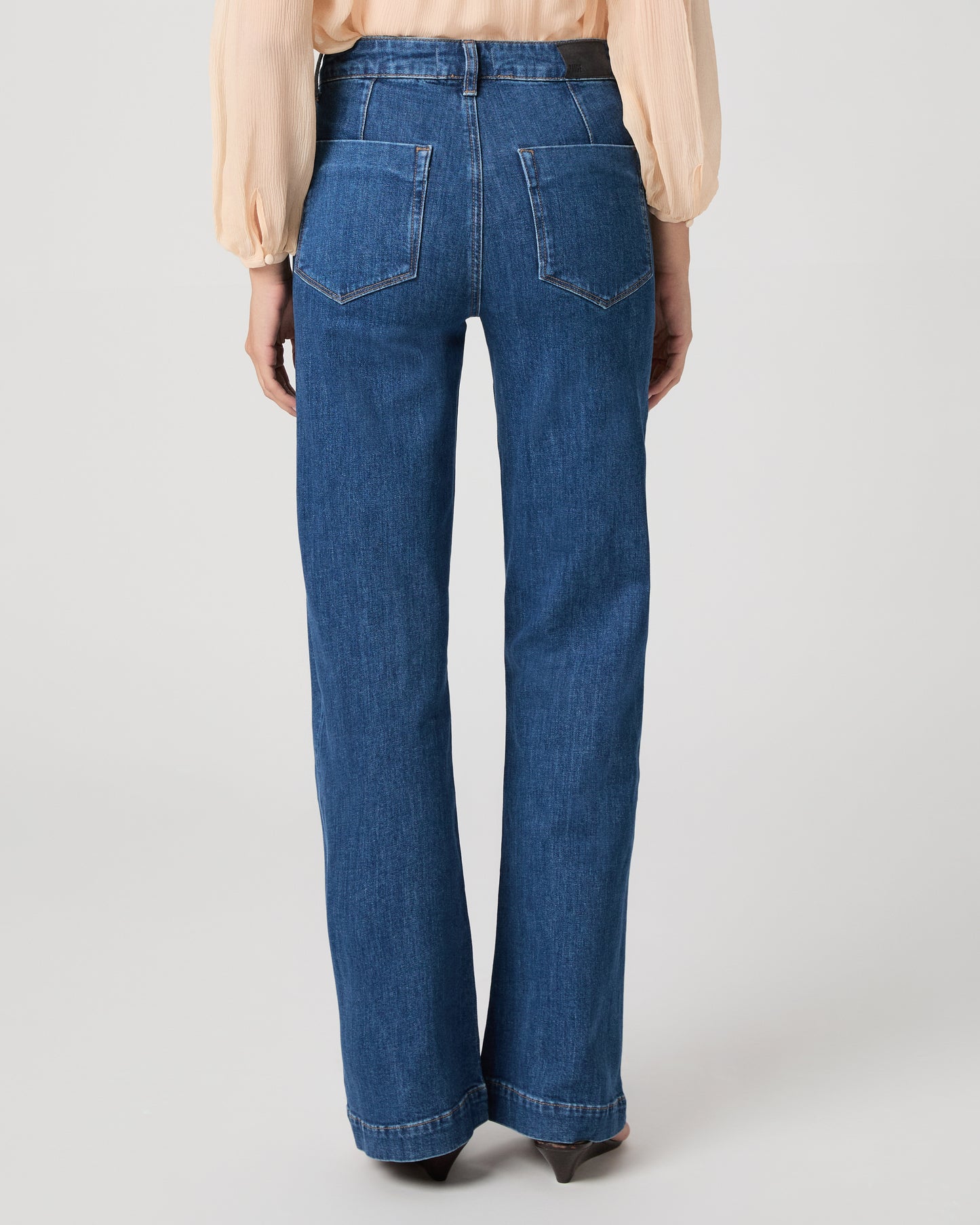 Women wearing light peach color blouse paired with medium wash denim against a white background