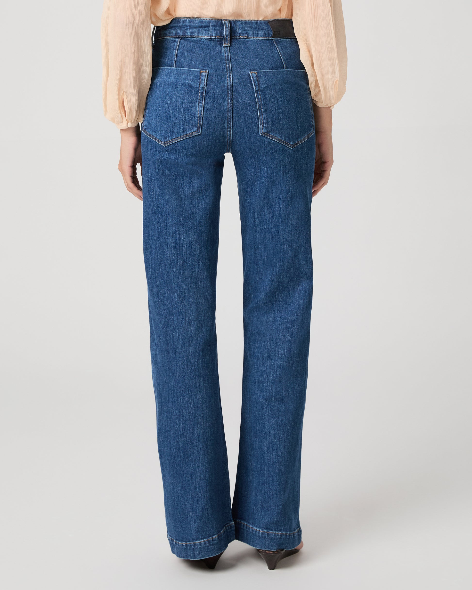 Women wearing light peach color blouse paired with medium wash denim against a white background