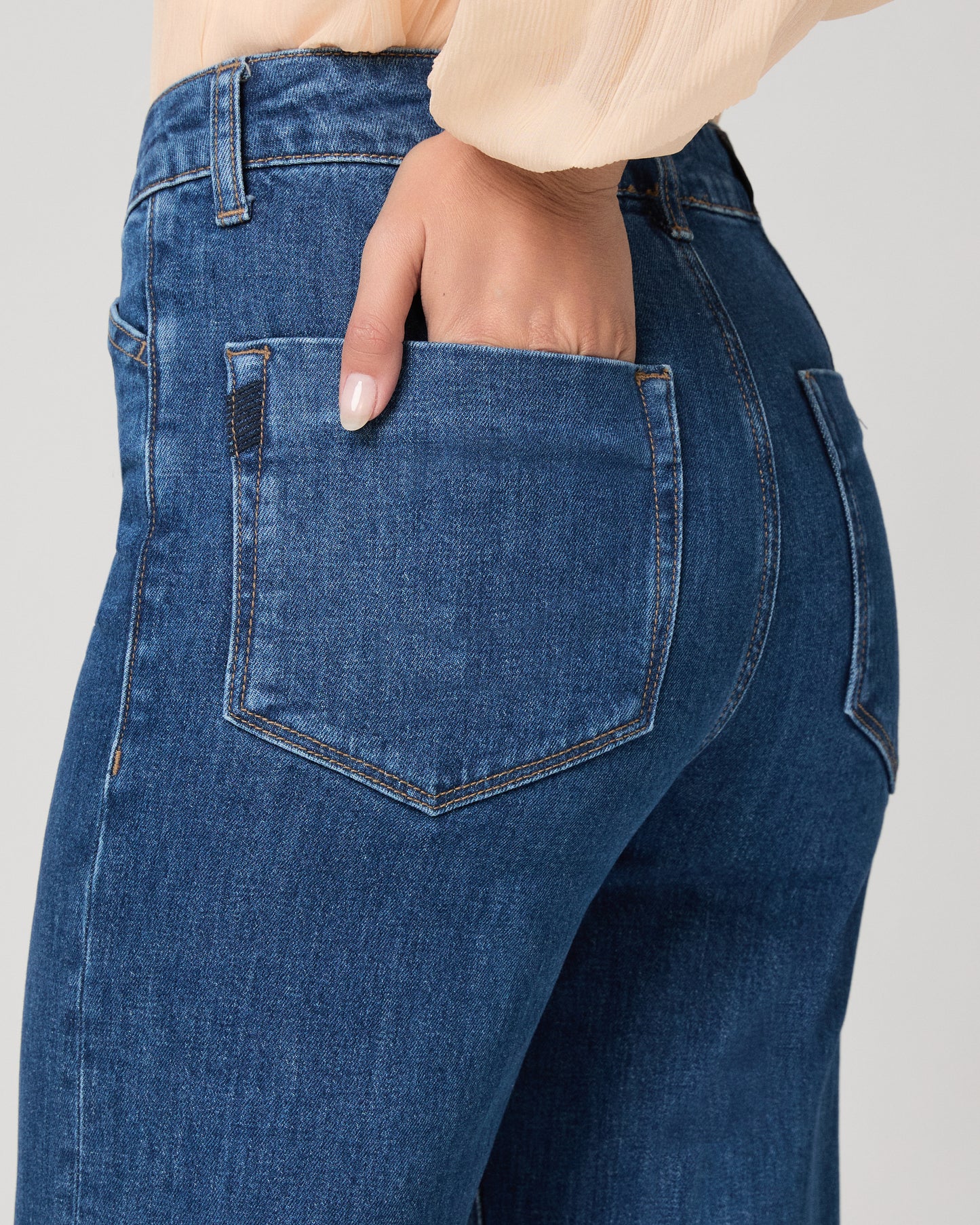 Women wearing light peach color blouse paired with medium wash denim against a white background