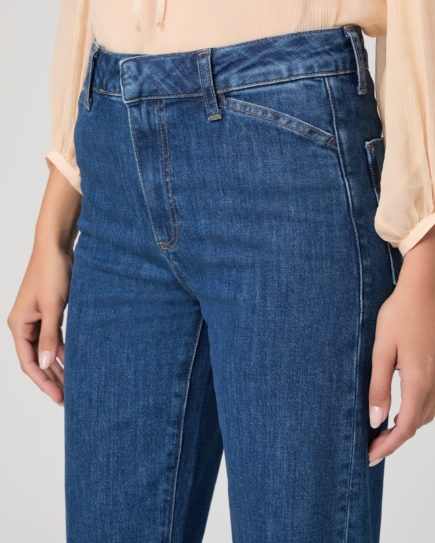 Women wearing light peach color blouse paired with medium wash denim against a white background