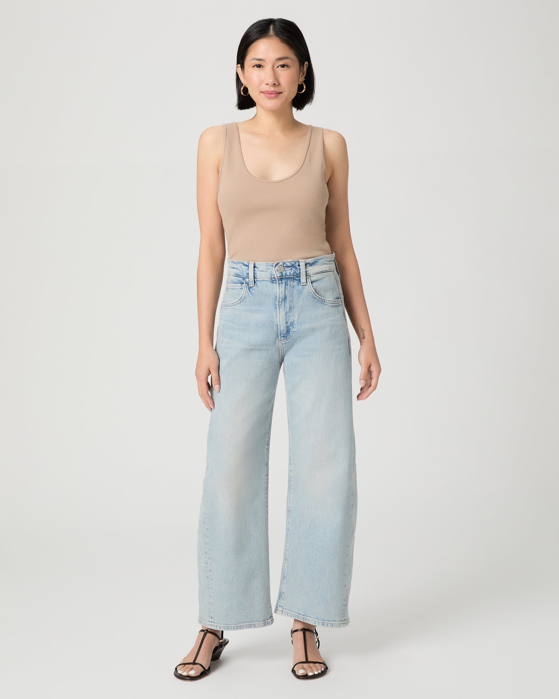 Woman wearing a beige tank top and light blue jeans on a white background