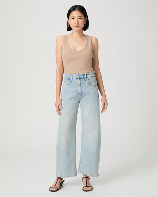 Woman wearing a beige tank top and light blue jeans on a white background