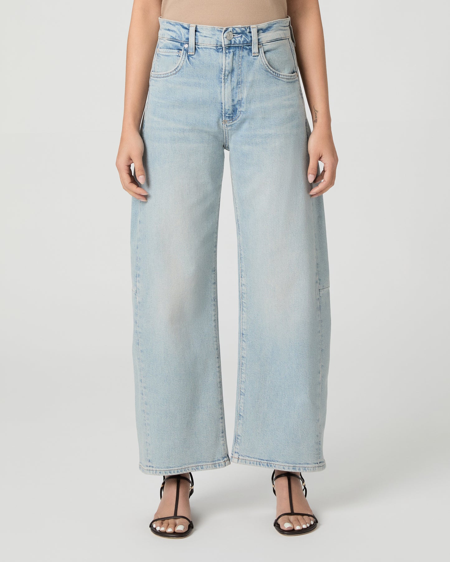 Woman wearing a beige tank top and light blue jeans on a white background