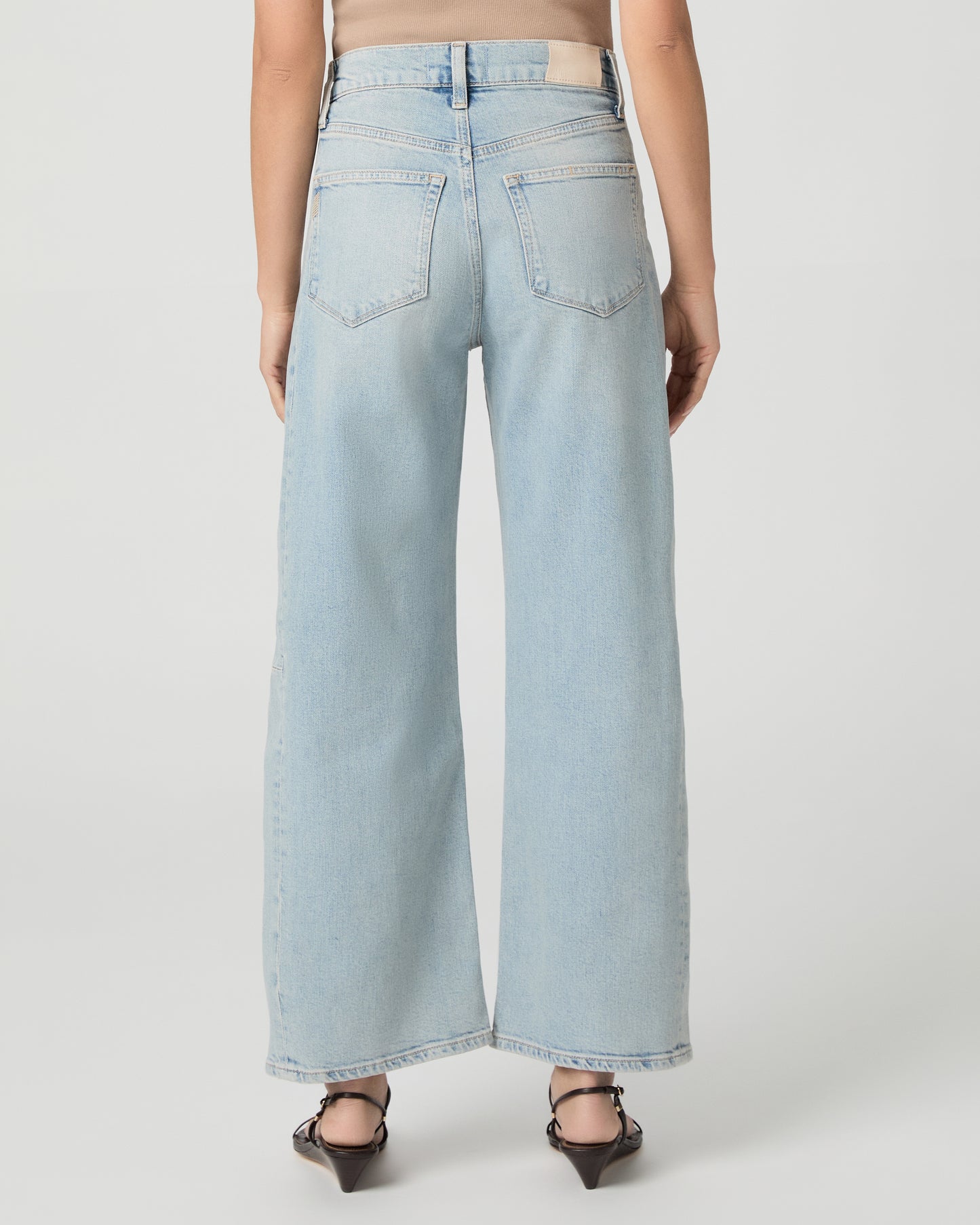 Woman wearing a beige tank top and light blue jeans on a white background