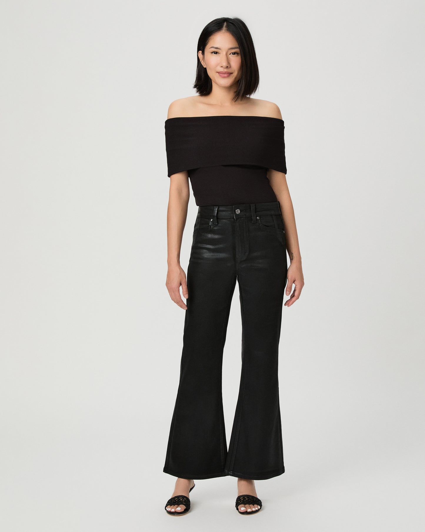 A woman modeling a black off-the-shoulder crop top and black wide-leg flare jeans against a light gray studio background.