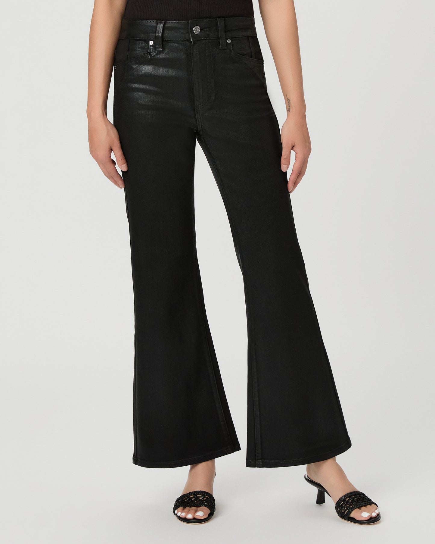A woman modeling a black off-the-shoulder crop top and black wide-leg flare jeans against a light gray studio background.