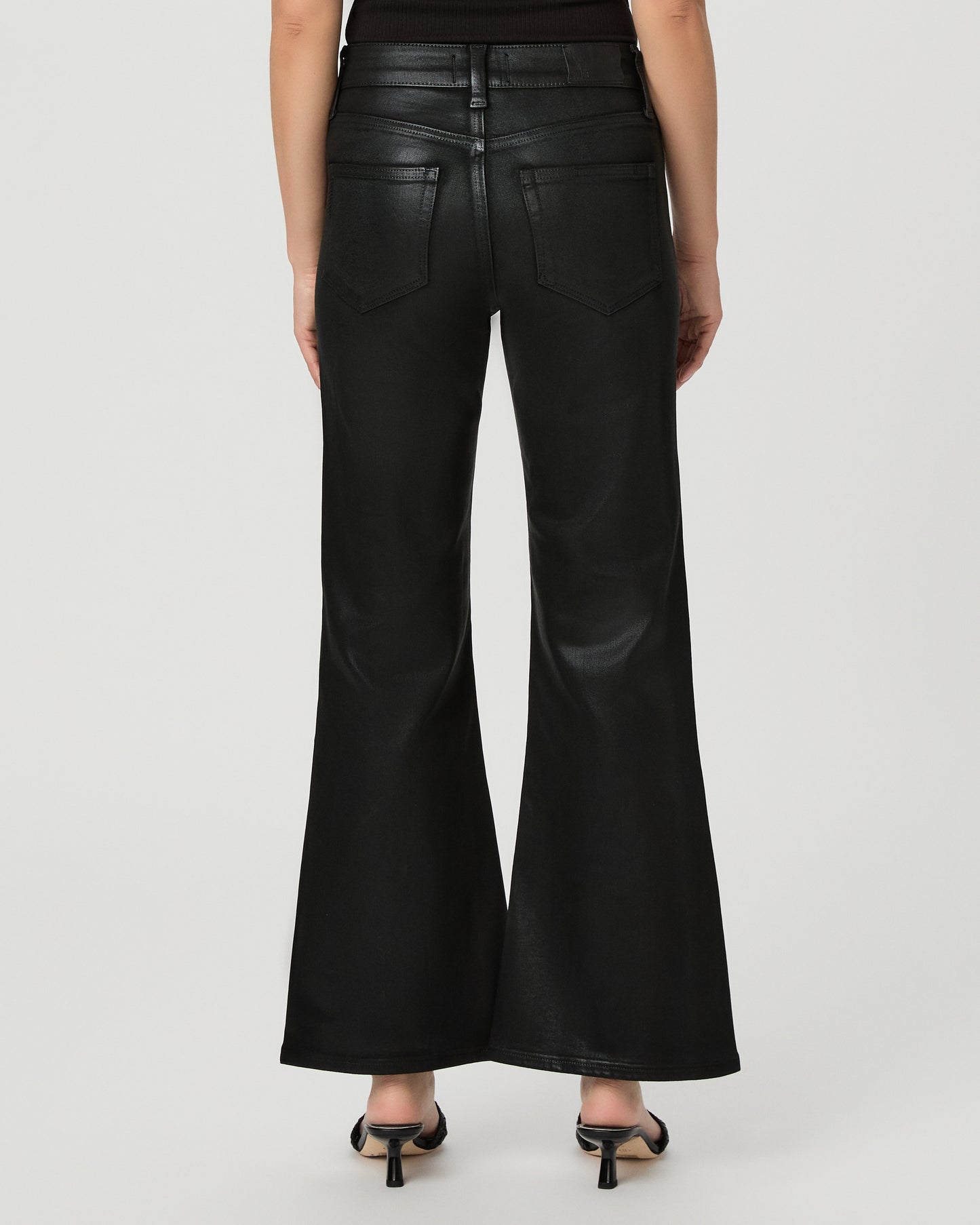A woman modeling a black off-the-shoulder crop top and black wide-leg flare jeans against a light gray studio background.