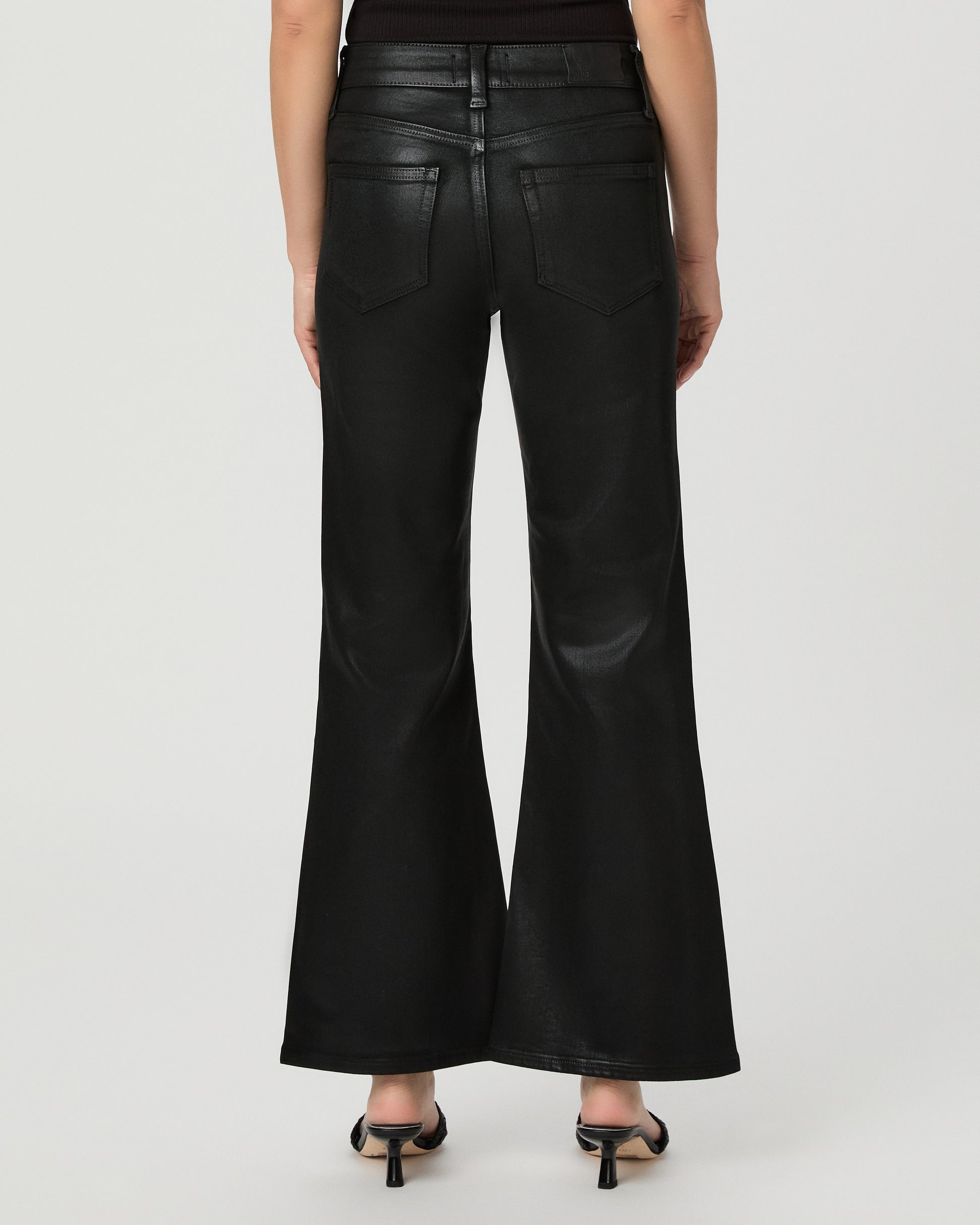 A woman modeling a black off-the-shoulder crop top and black wide-leg flare jeans against a light gray studio background.