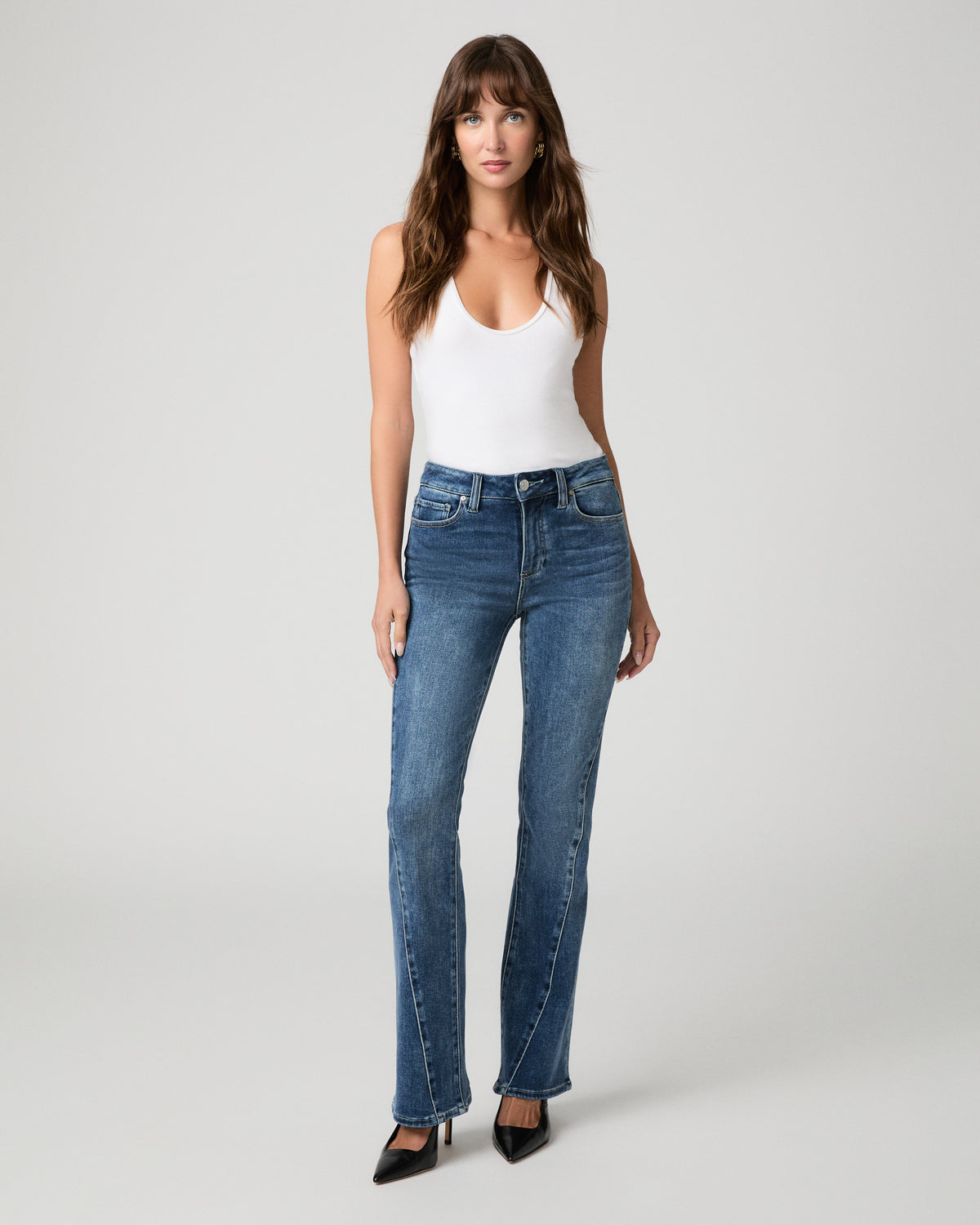 Woman wearing white top and blue pants against a white background