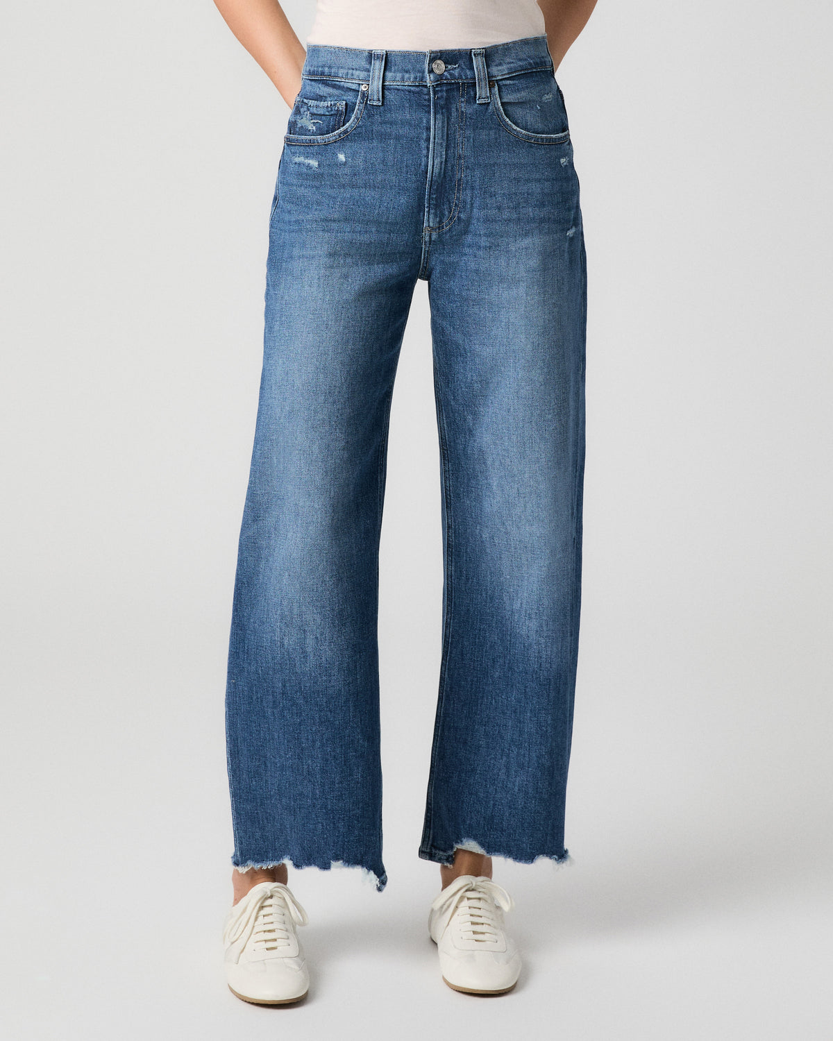 Front view from the waist down of the Arellia Ankle Barrel Leg Jean in Stoneview medium wash, showing light distressing and a frayed hem, with white sneakers