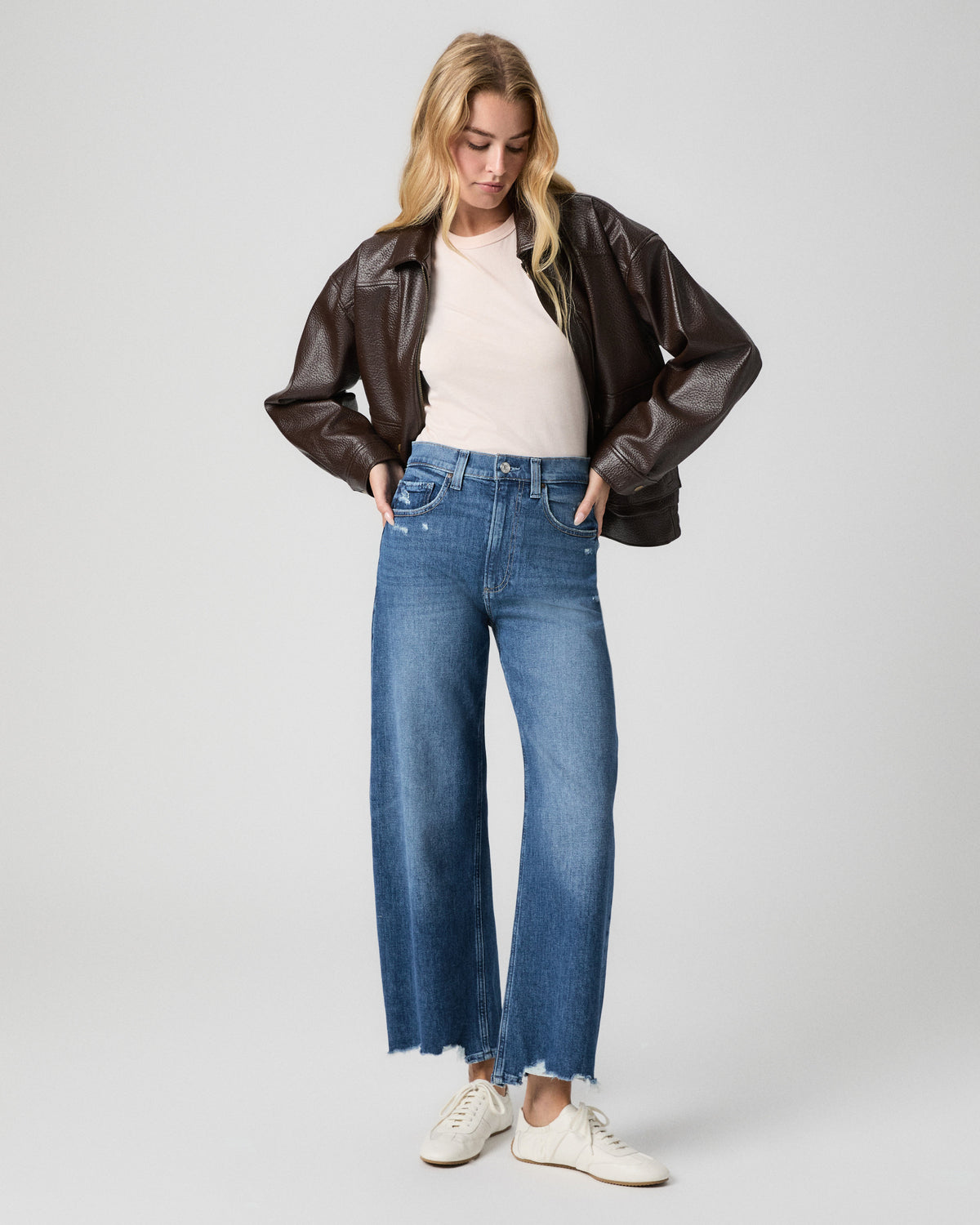 Arellia Ankle Barrel Leg Jean in Stoneview medium wash; model stands with hands in her pockets, in a brown leather jacket, cream tee and white sneakers