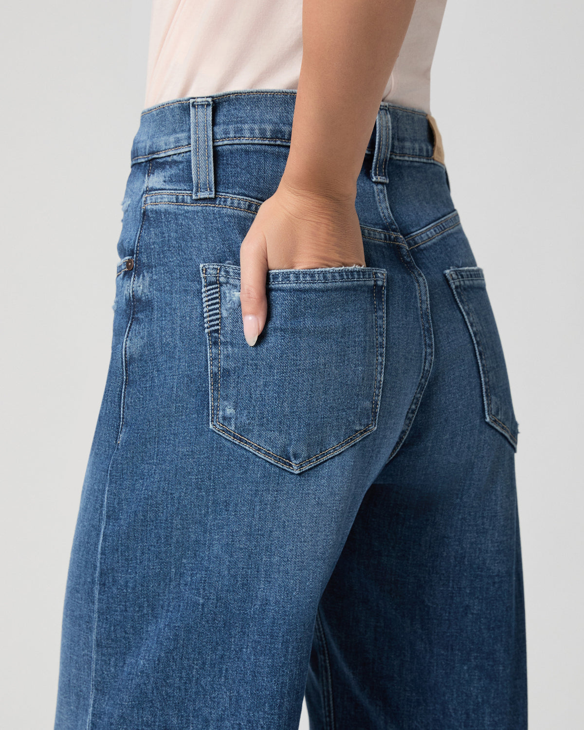 Close-up of the back pocket of the Arellia Ankle Barrel Leg Jean in Stoneview medium wash; model has one hand in the pocket
