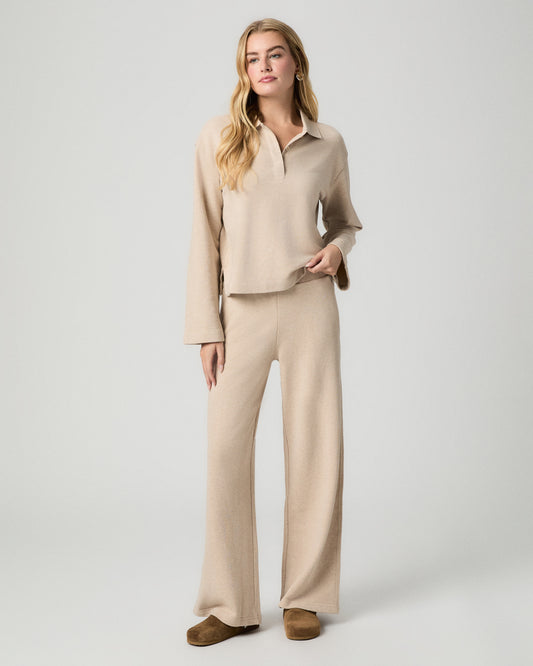 Full-length view of model with one hand in her pocket, wearing the Whistler Pant in Heathered Oatmeal, a wide-leg knit pant, with a matching collared knit top and brown suede clogs