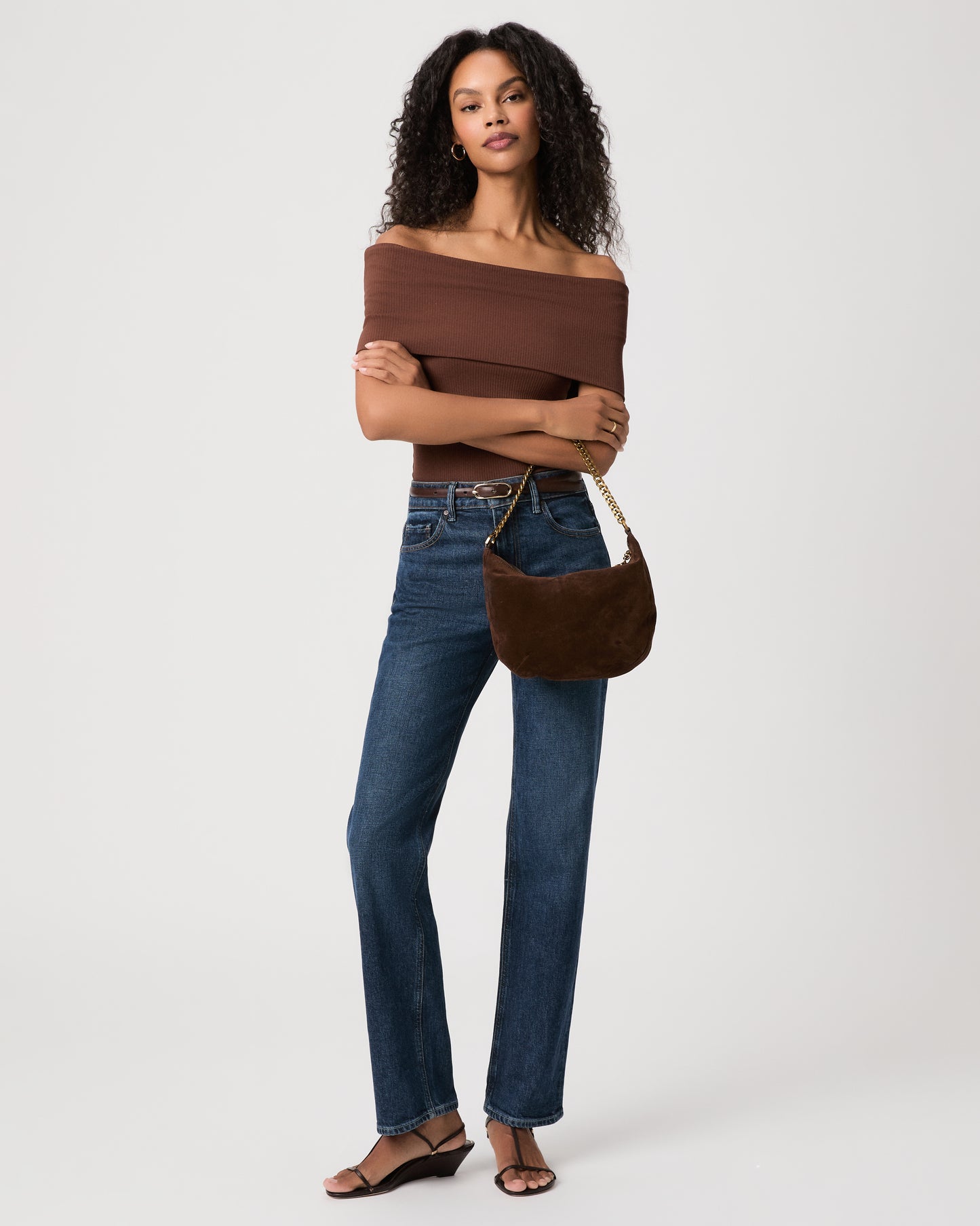 Women wearing brown top paired with blue jeans holding a brown green bag against a white background 