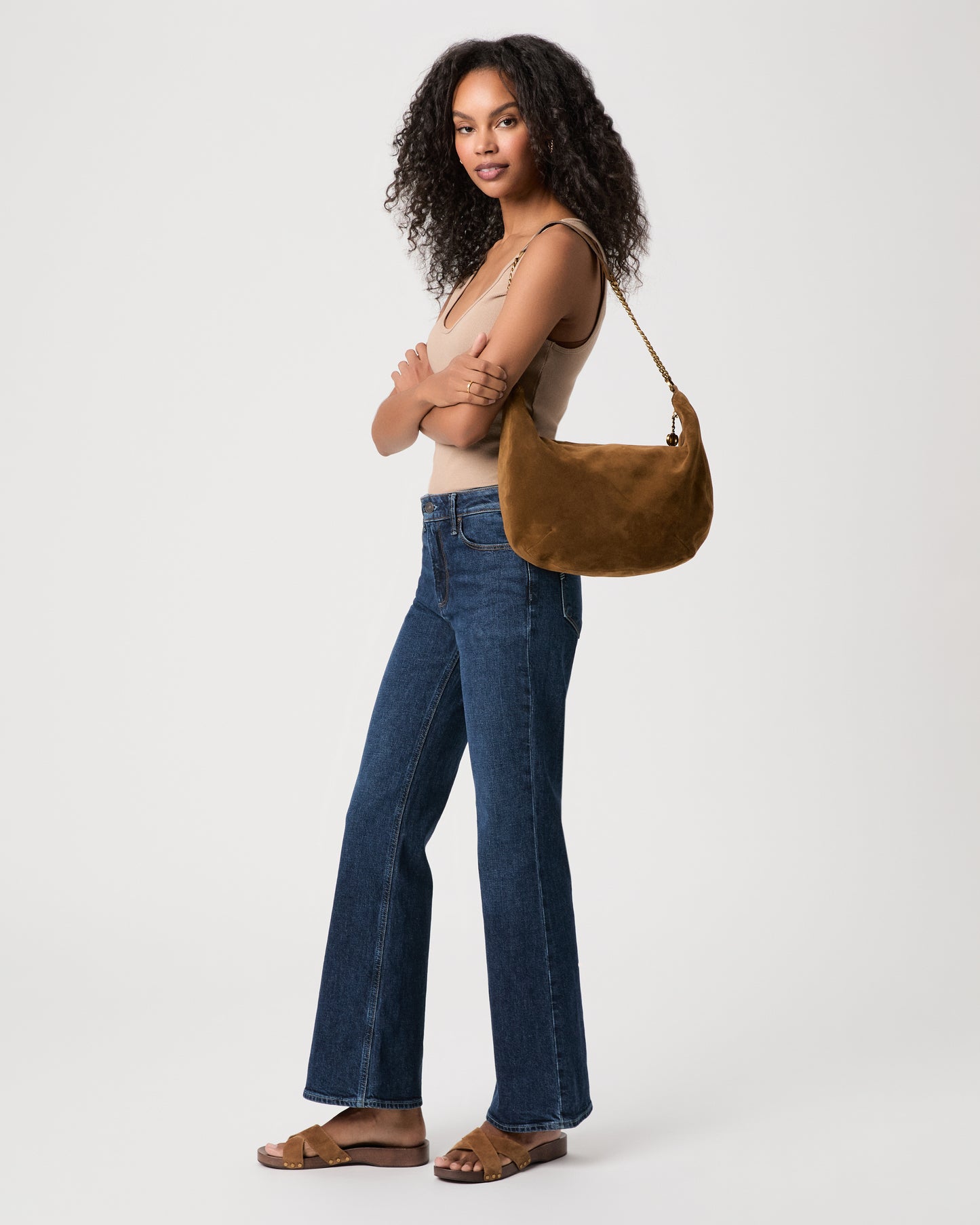 women wearing brown top Paired with blue jeans holding a brown suede bag against a white background 