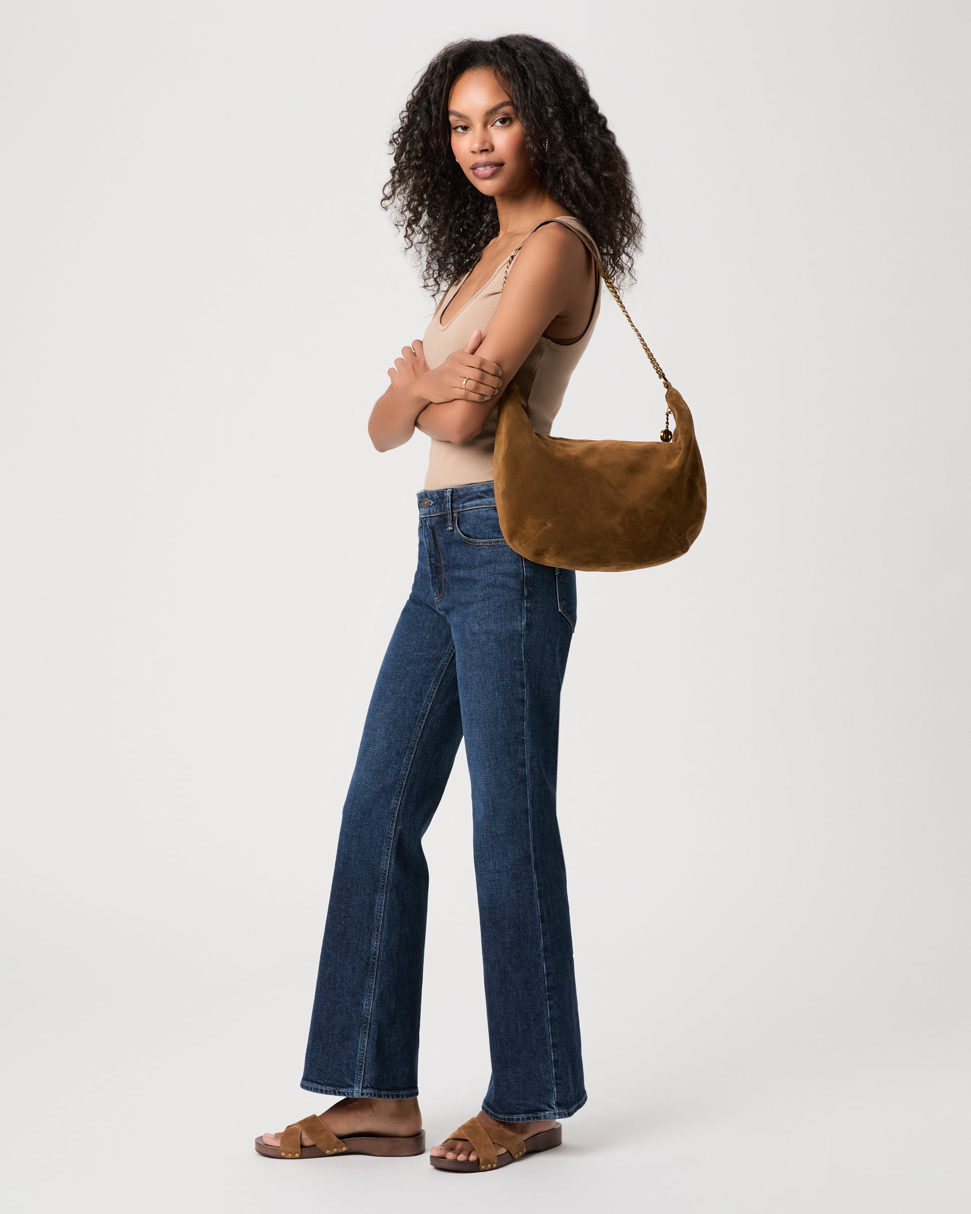 women wearing brown top Paired with blue jeans holding a brown suede bag against a white background 