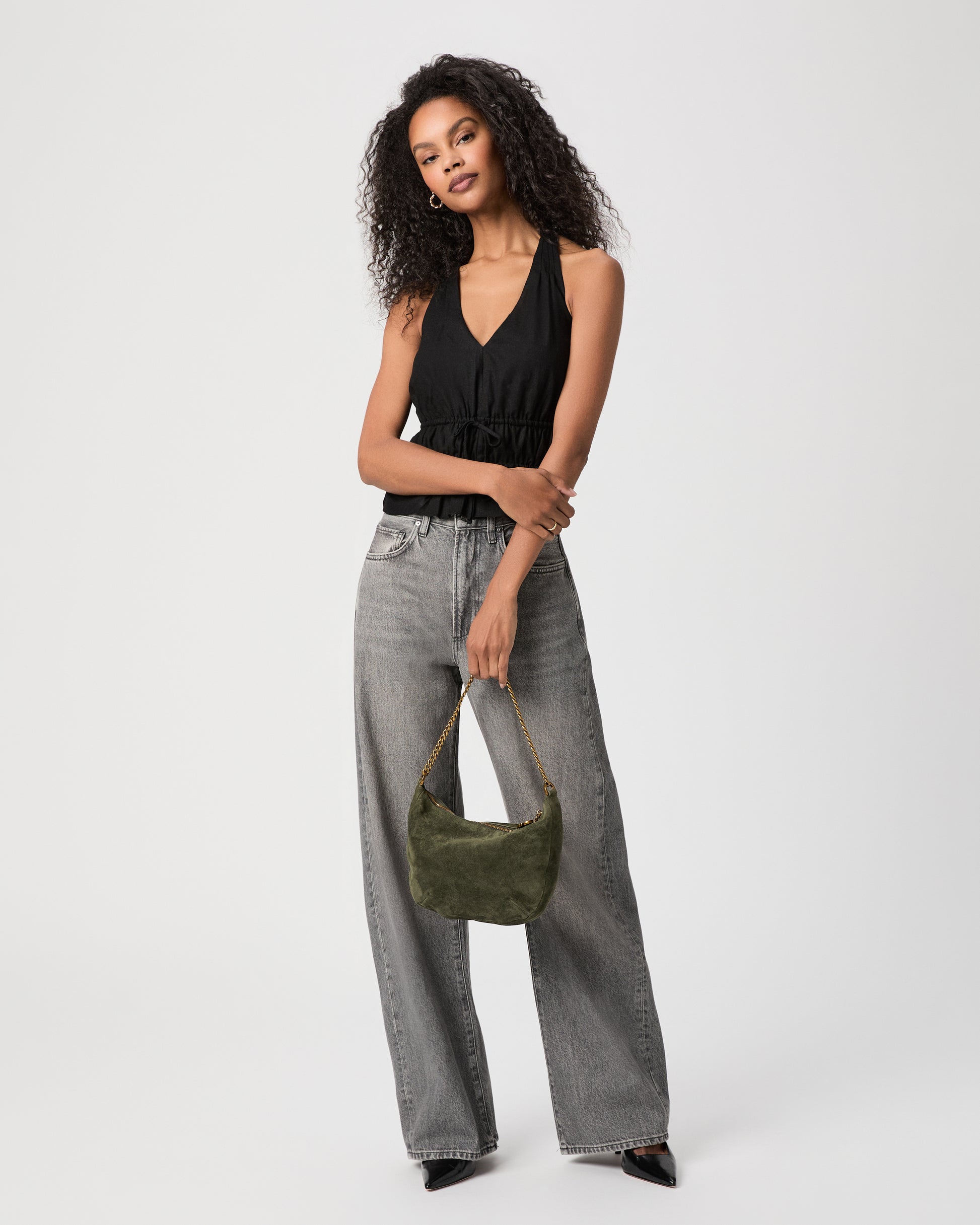 Women wearing black top paired with grey jeans holding a suede green bag against a white background 