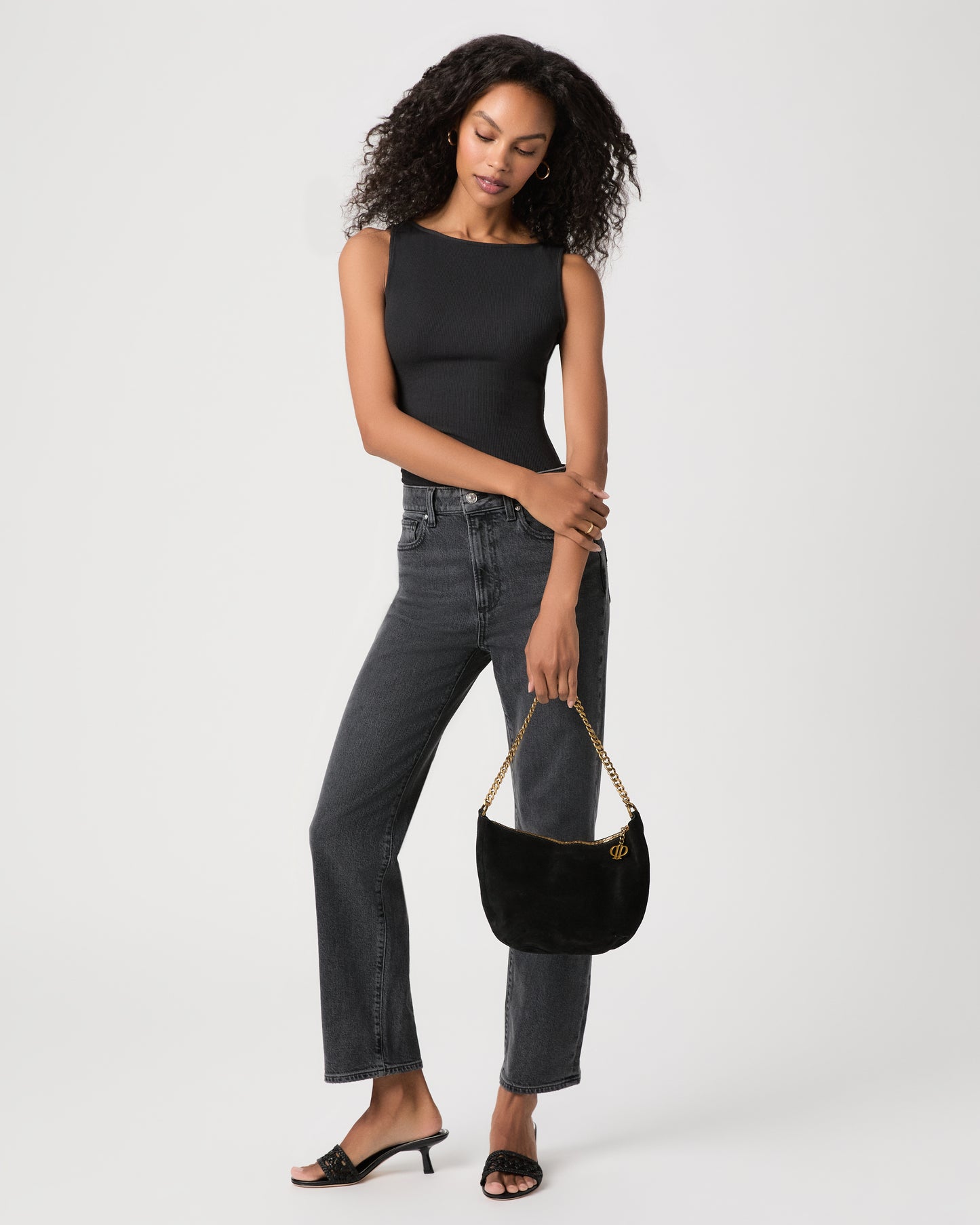 women wearing black top Paired with black jeans holding a black suede bag against a white background 