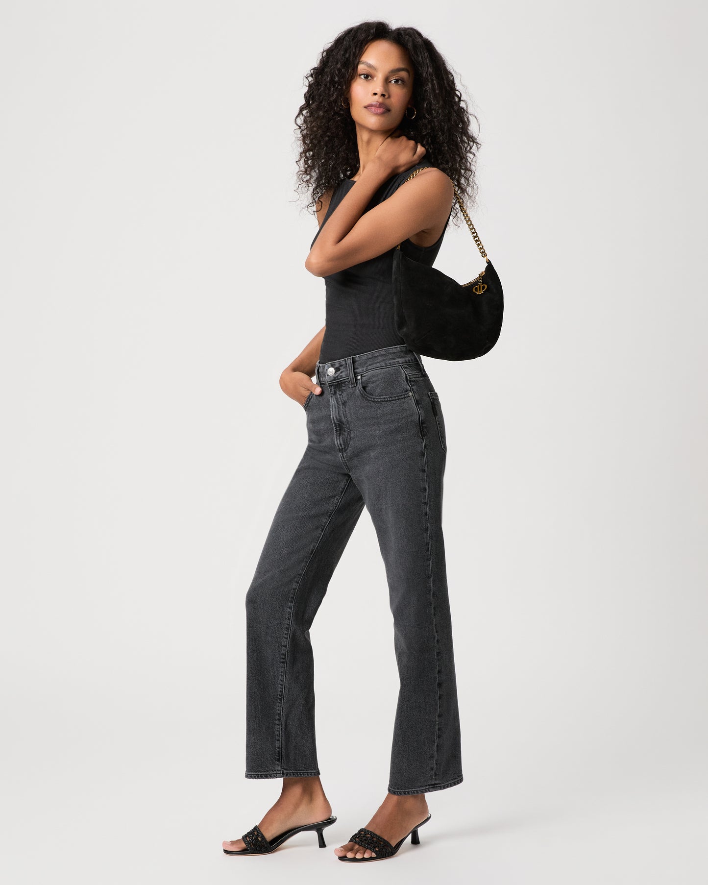 women wearing black top Paired with black jeans holding a black suede bag against a white background 