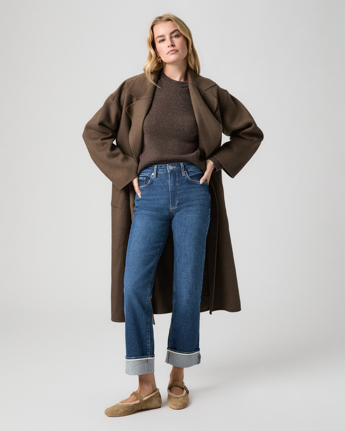 Stevie Straight Jean in Soundcheck dark wash with wide cuffs; model stands with hands in her pockets, in a long brown coat, brown sweater and tan suede flats