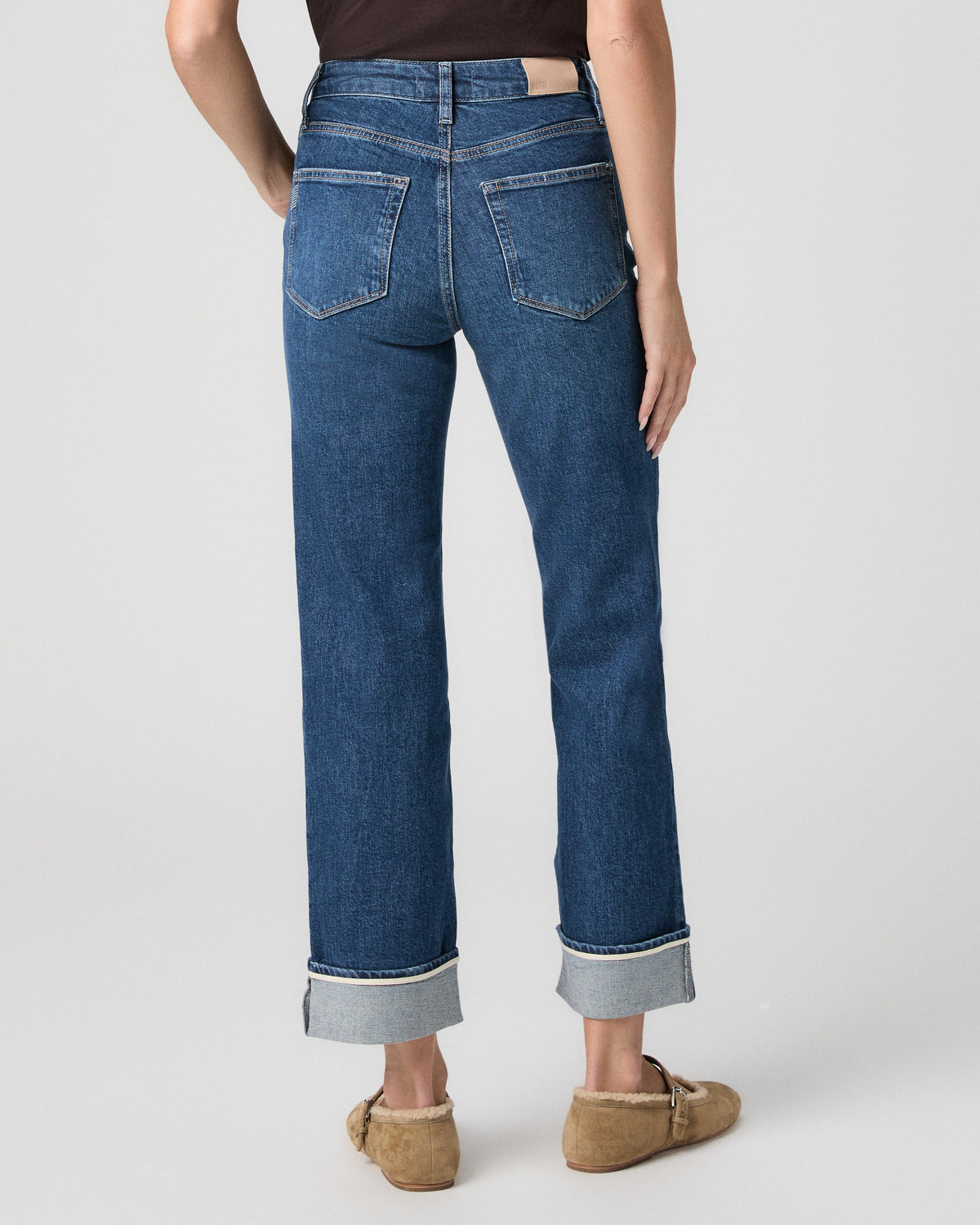 Back view from the waist down of the Stevie Straight Jean in Soundcheck dark wash, showing the wide cuffs, with tan suede flats