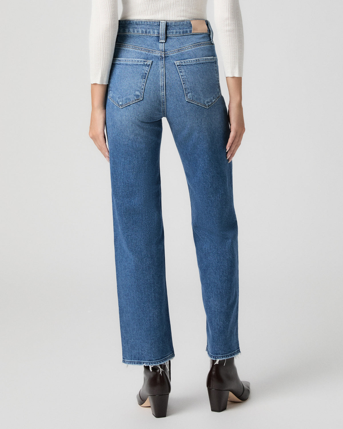 Back view from the waist down of the Stevie Ankle Straight Jean in Frittata Dest light-medium wash, worn with a white top and black ankle boots