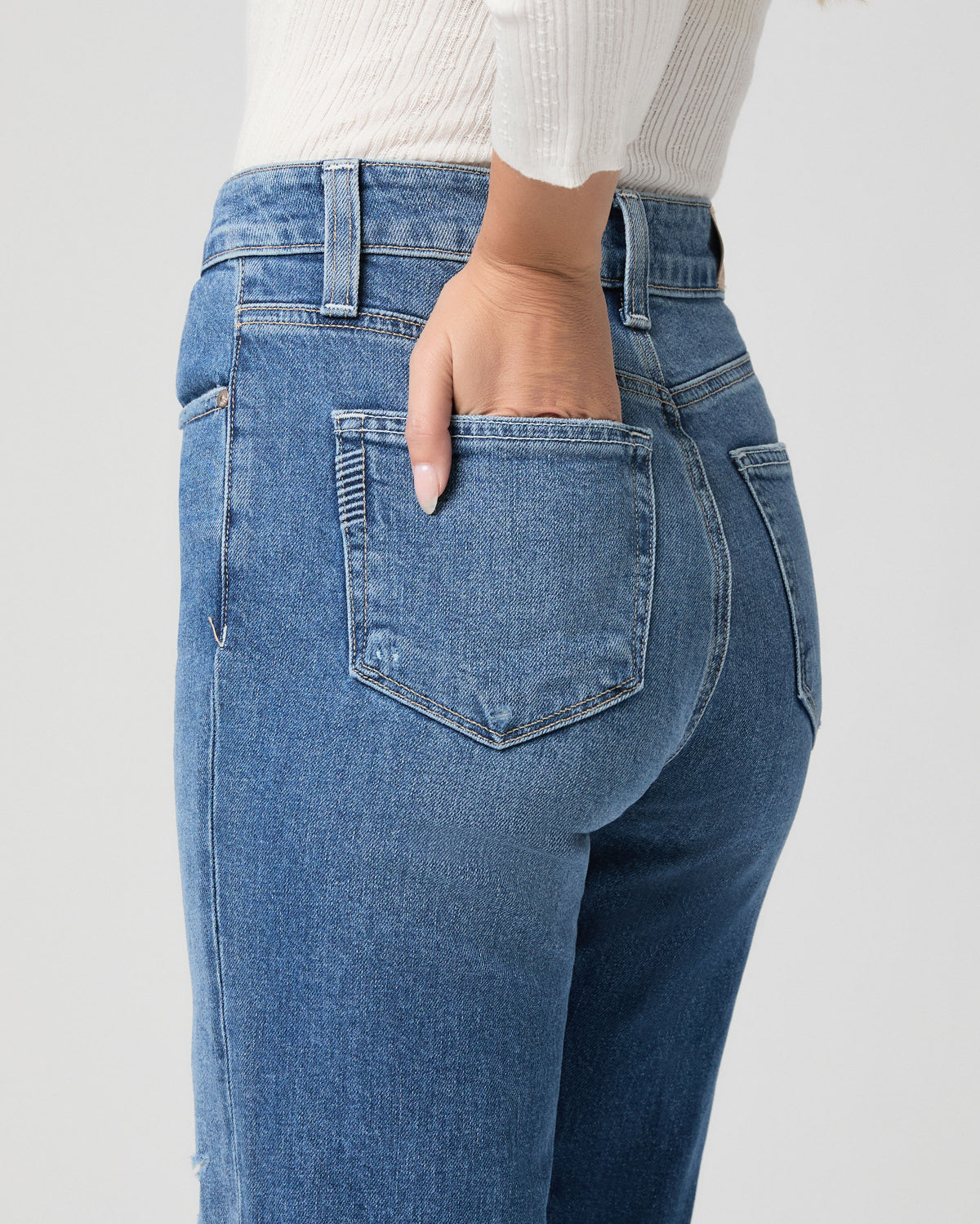 Close-up of the back pocket of the Stevie Ankle Straight Jean in Frittata Dest light-medium wash; model has one hand in the pocket and wears a white top