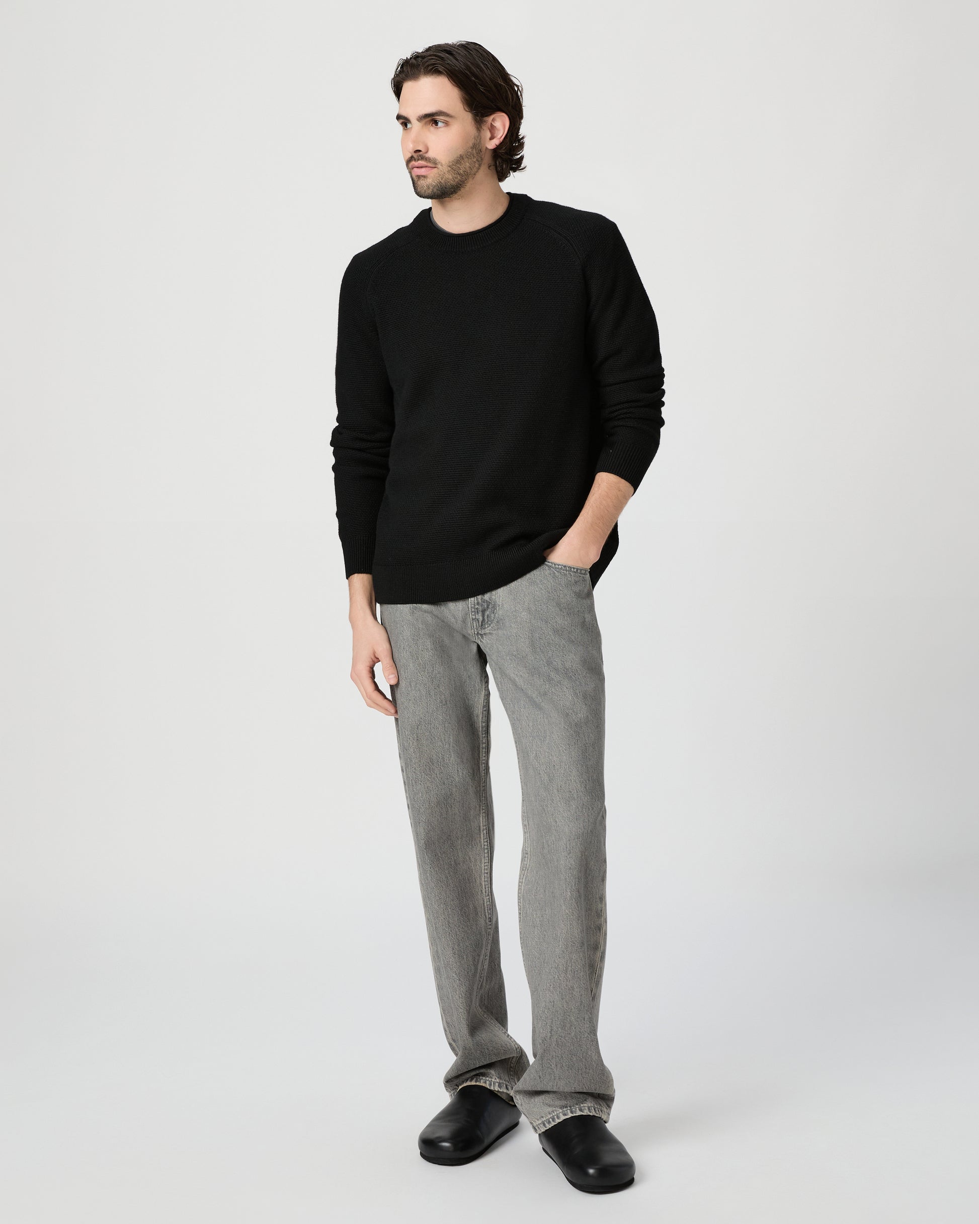 Man wearing a black sweater and gray pants on a white background
