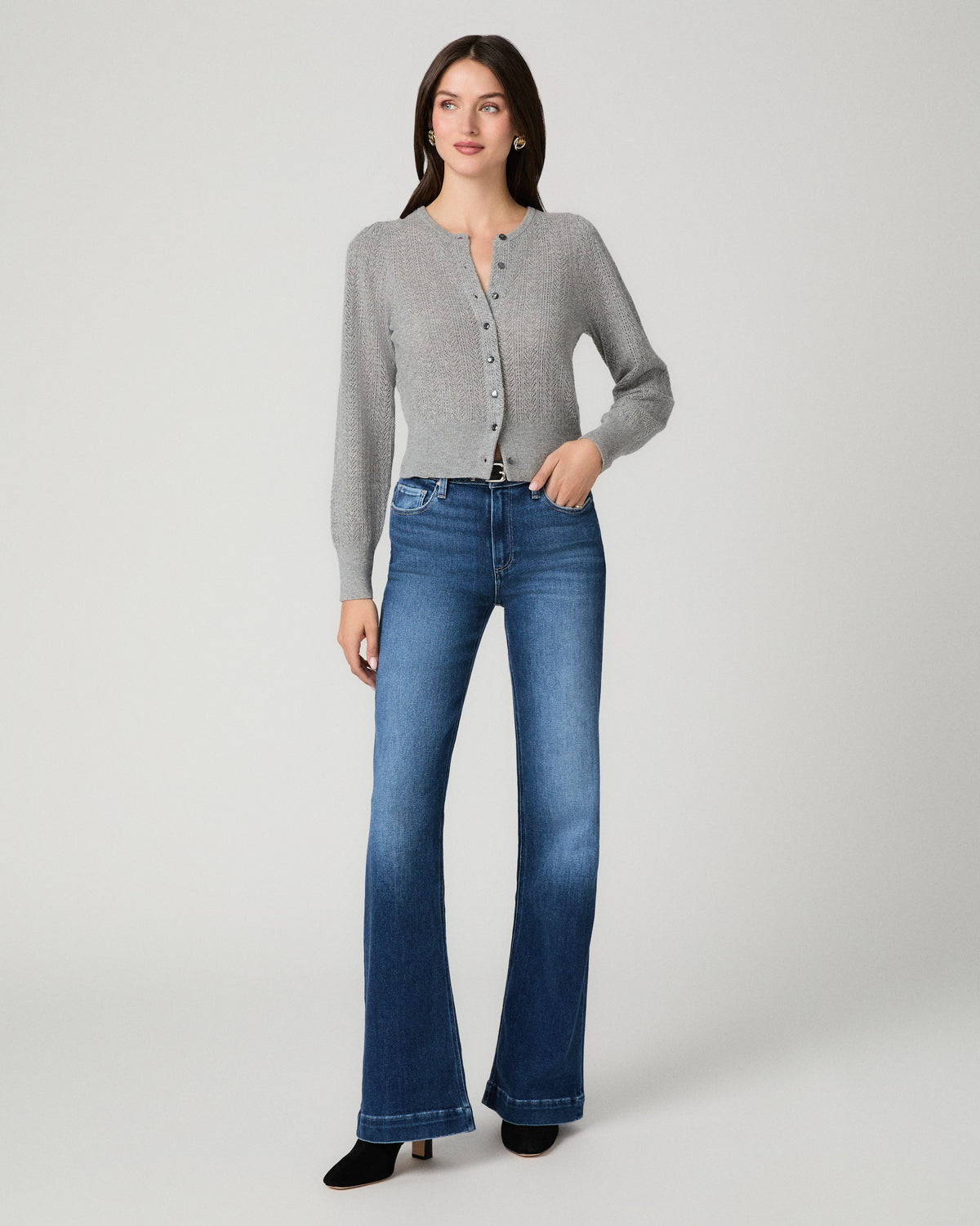 A woman modeling a light gray long-sleeve button-front cardigan and blue high-waisted flare jeans against a plain light gray studio background.
