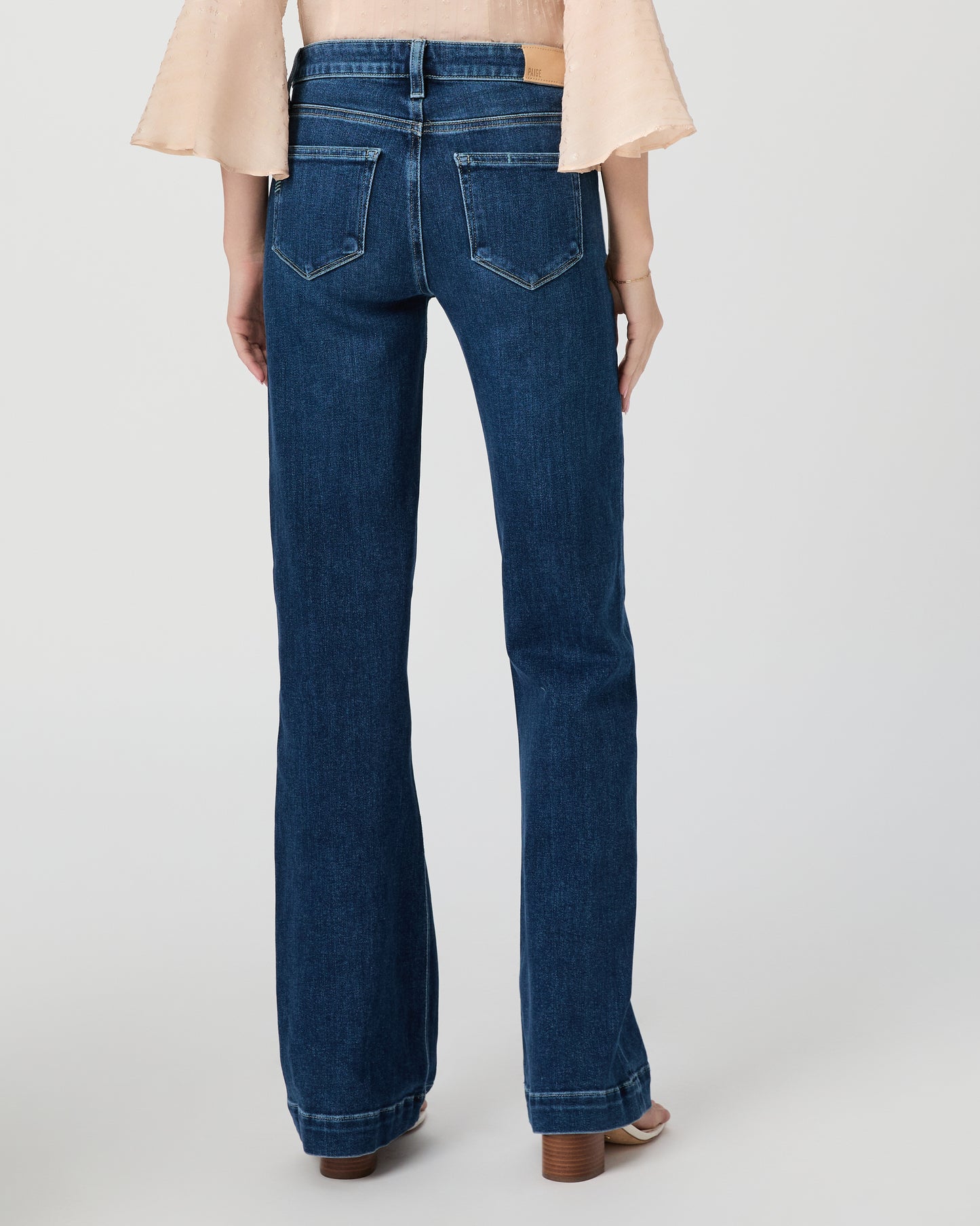 Woman wearing a beige blouse and blue jeans paired with white sandals on a white background