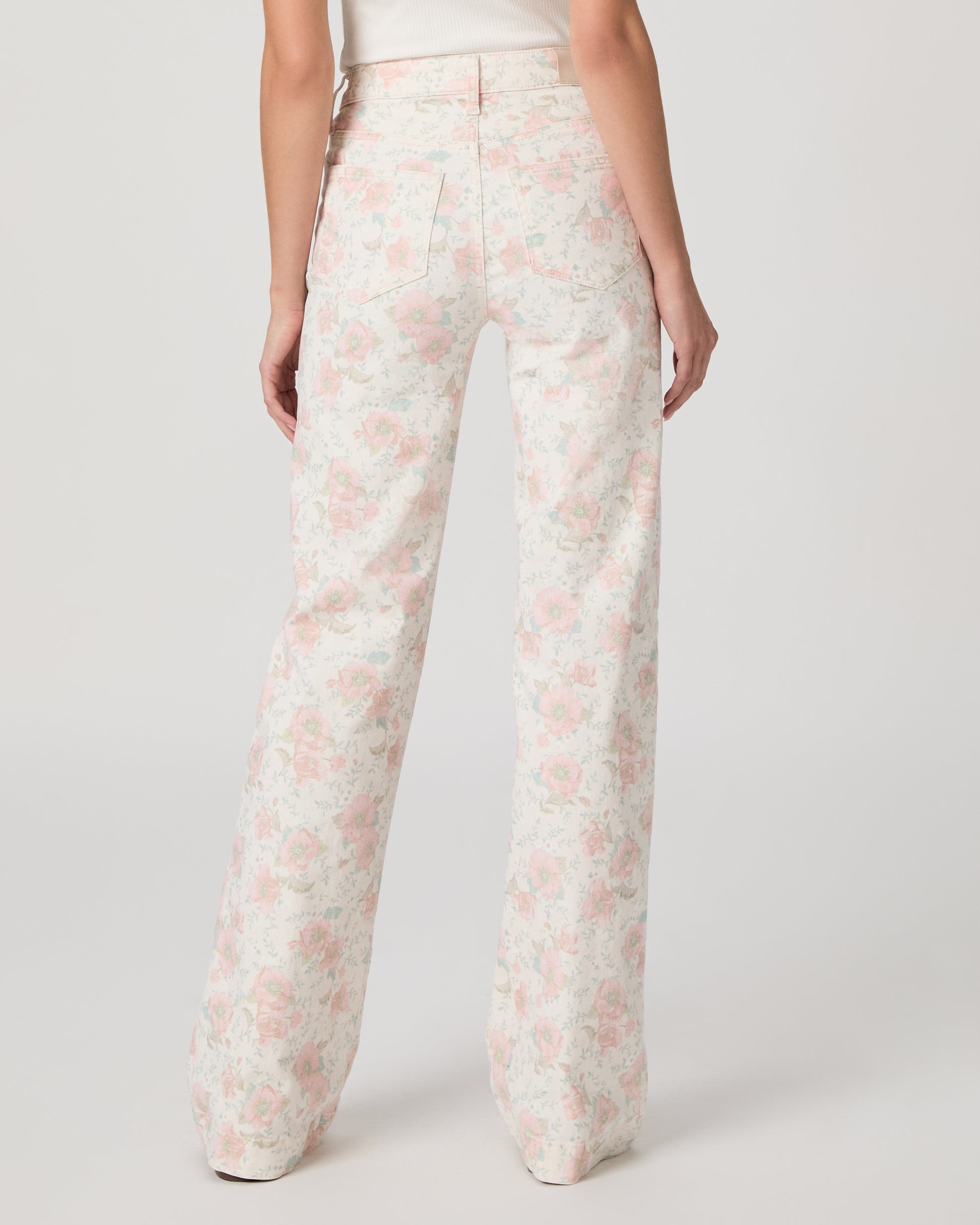 Woman wearing a white top and flower printed jeans paired with white sandals on a white background