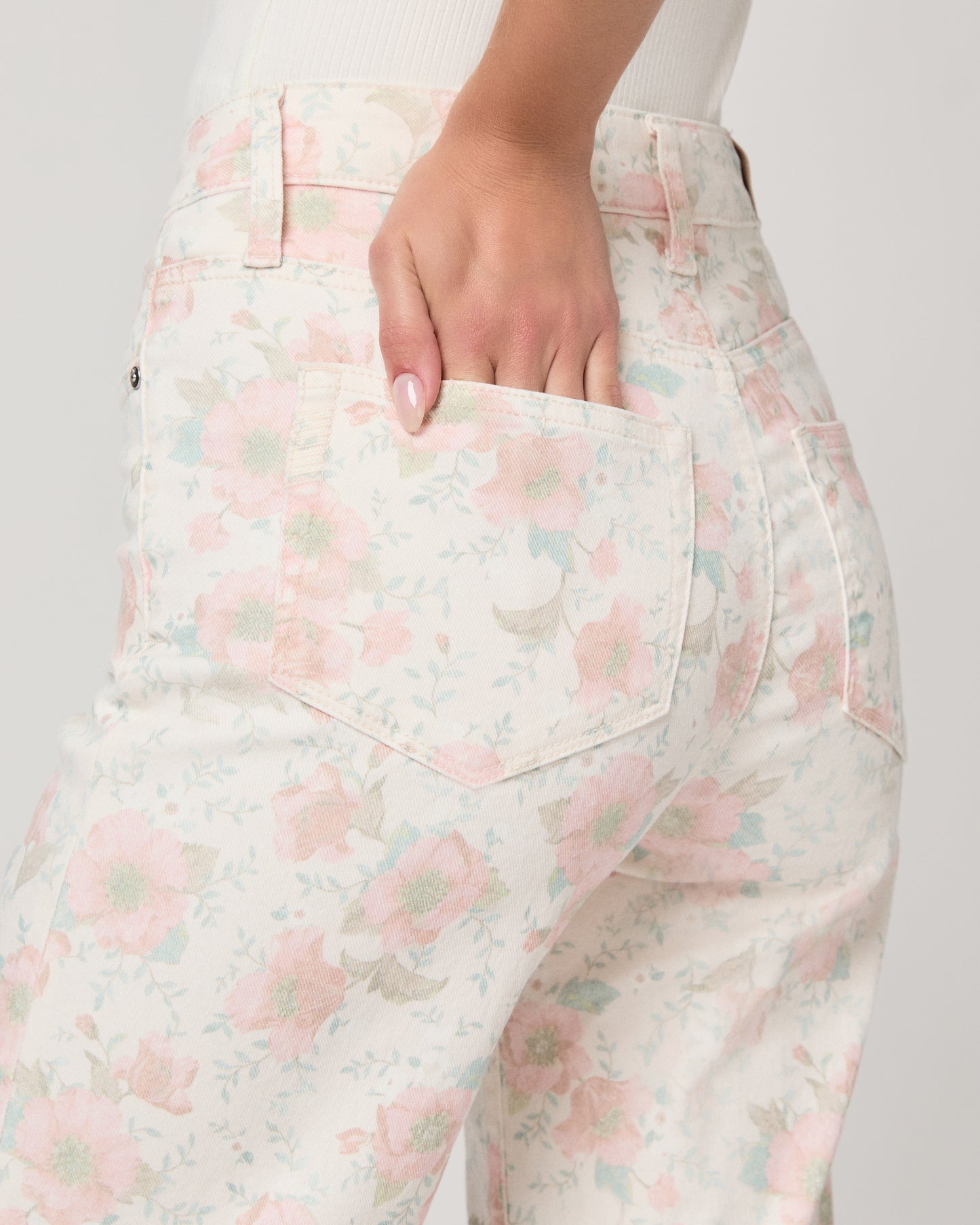 Woman wearing a white top and flower printed jeans paired with white sandals on a white background