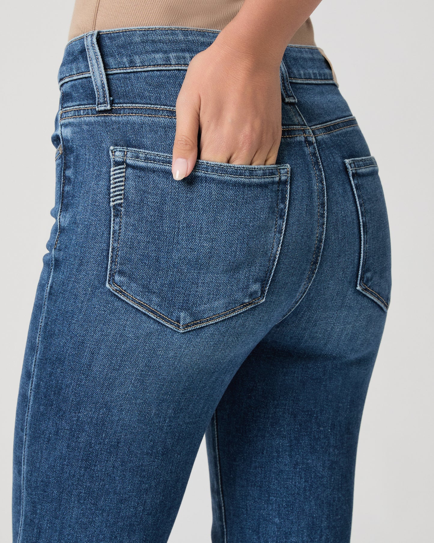 Woman wearing a white textured cardigan, beige top, and blue jeans on a white background