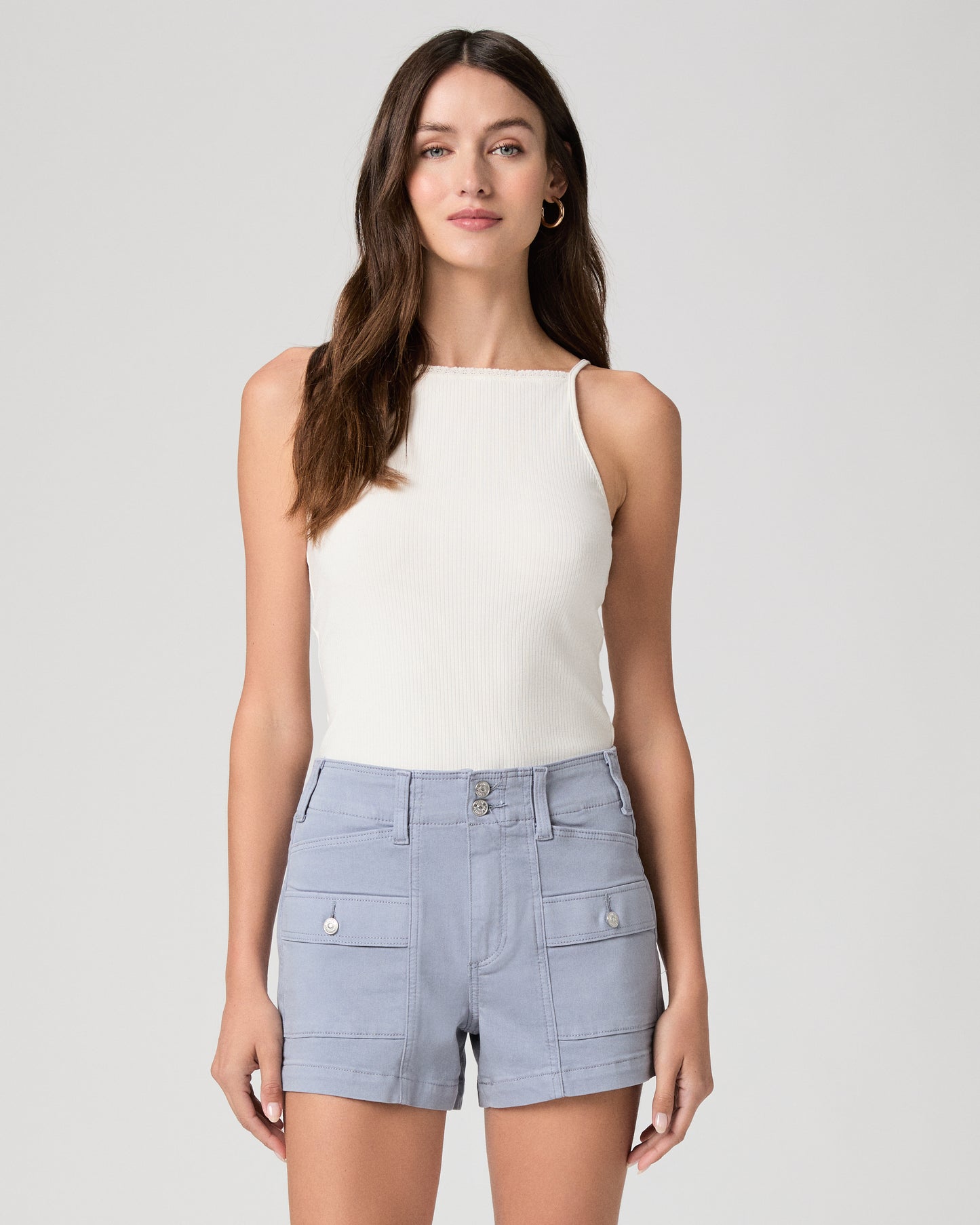 Woman wearing a white sleeveless top and light blue shorts on a white background