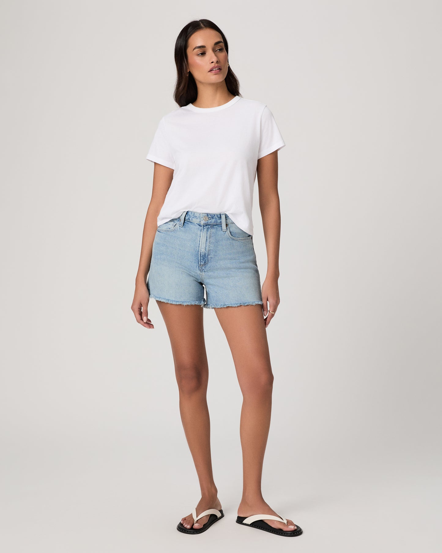 Women wearing a white tee and light wash shorts paired with black sandal with white strap on a light gray background