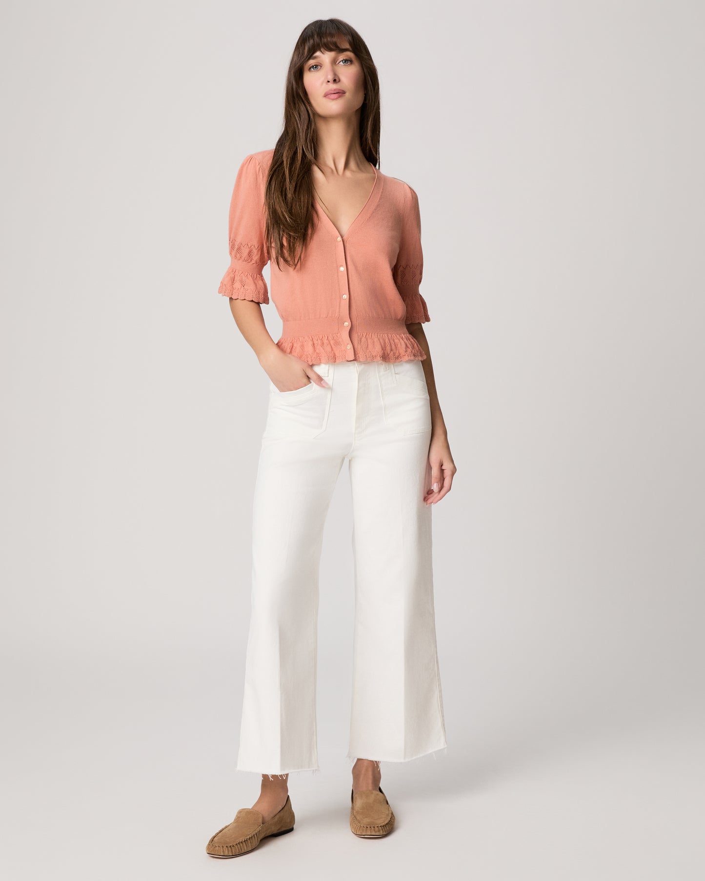 Woman wearing a pink blouse and white pants on a plain background