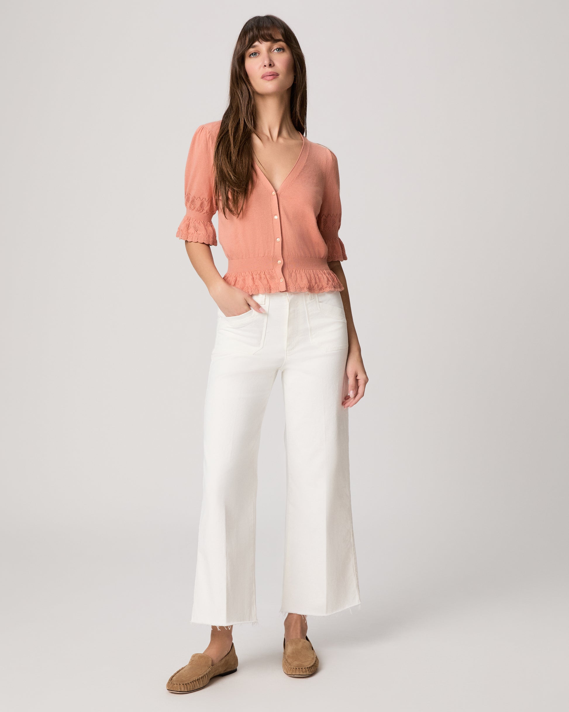 Woman wearing a pink blouse and white pants on a plain background