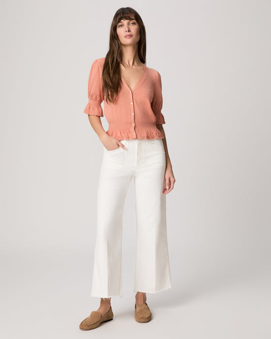 Woman wearing a pink blouse and white pants on a plain background