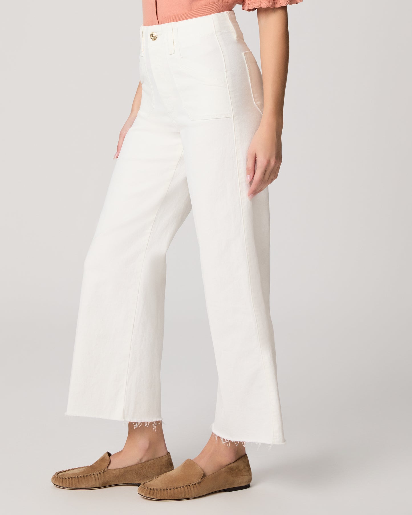 Person wearing white pants and brown loafers on a plain background