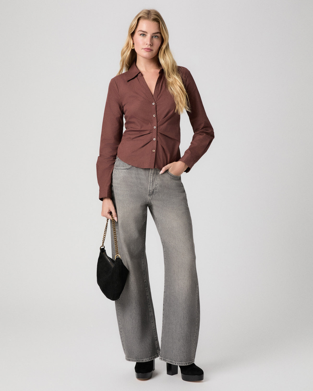 Alera Shirt in French Press brown; model stands with a hand in her pocket, holding a black shoulder bag, with grey wide leg jeans and black heels