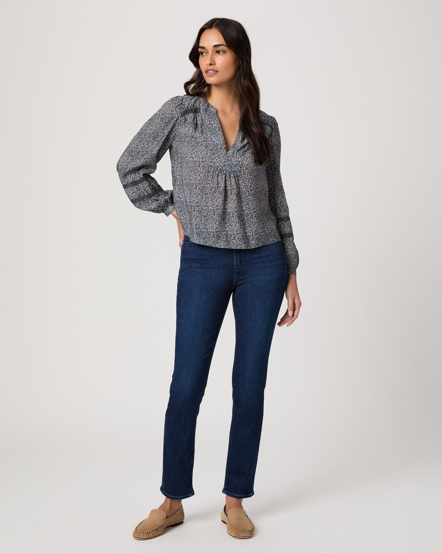 Woman wearing a blue patterned blouse and blue jeans on a white background