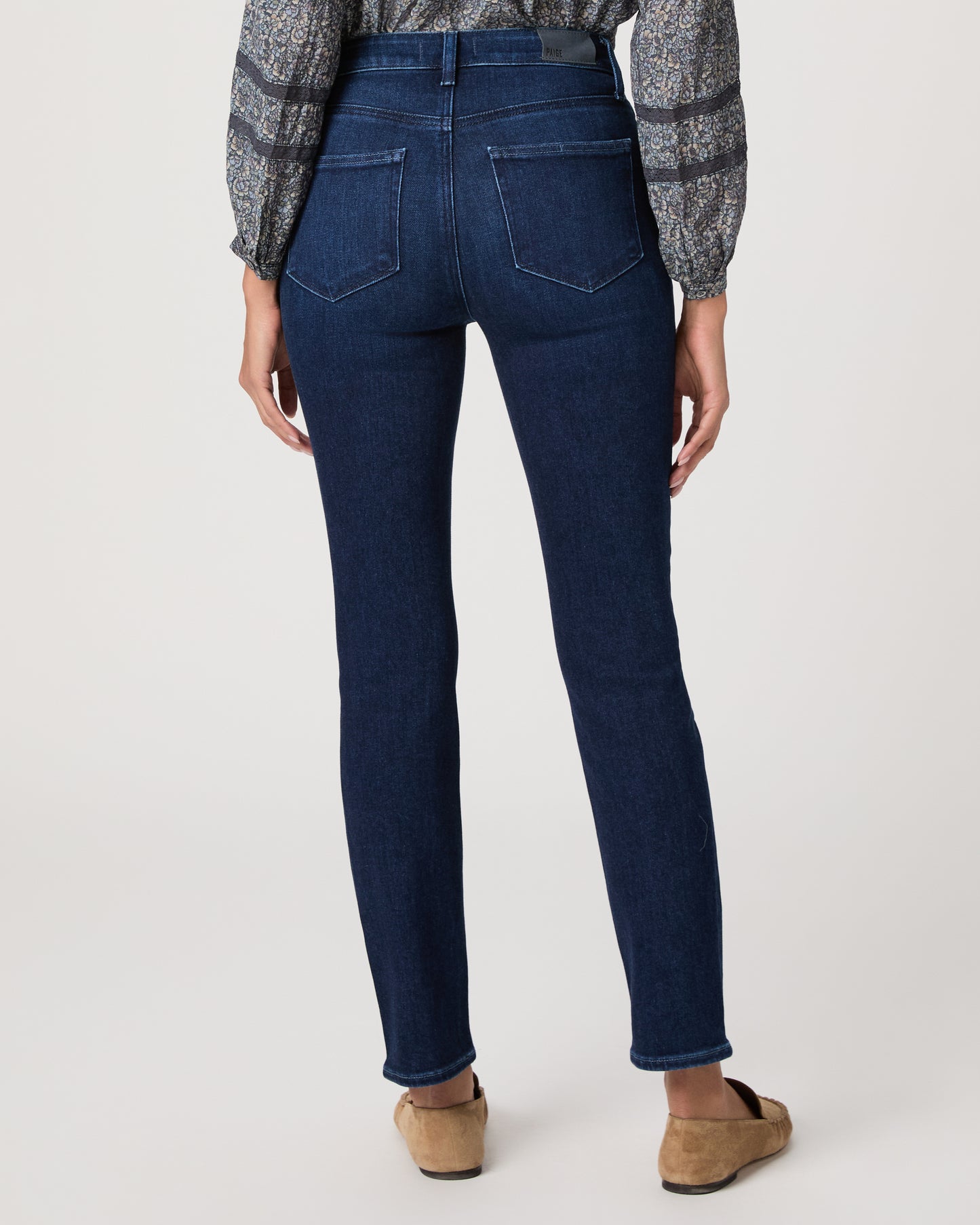 Woman wearing a blue patterned blouse and blue jeans on a white background