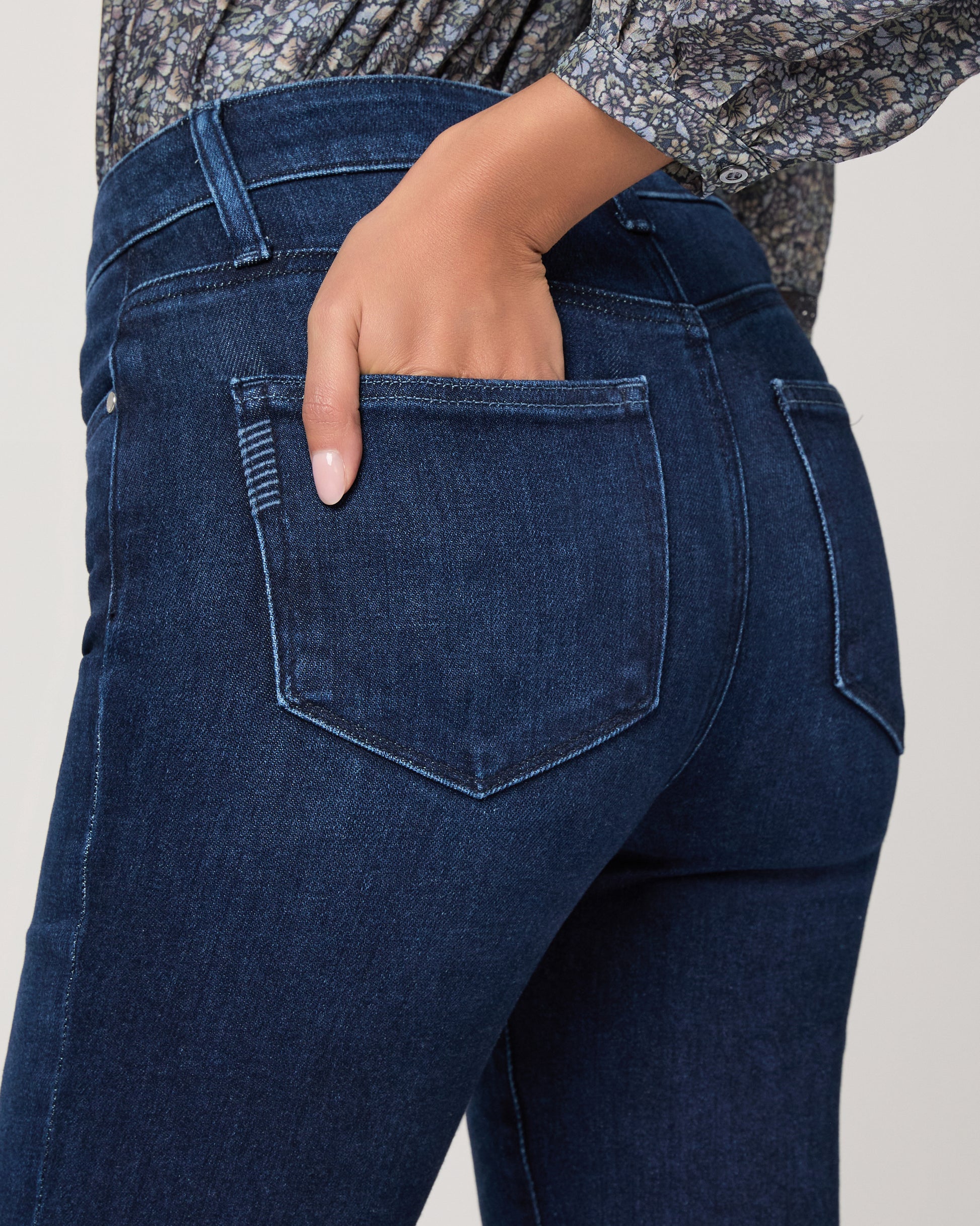 Woman wearing a blue patterned blouse and blue jeans on a white background