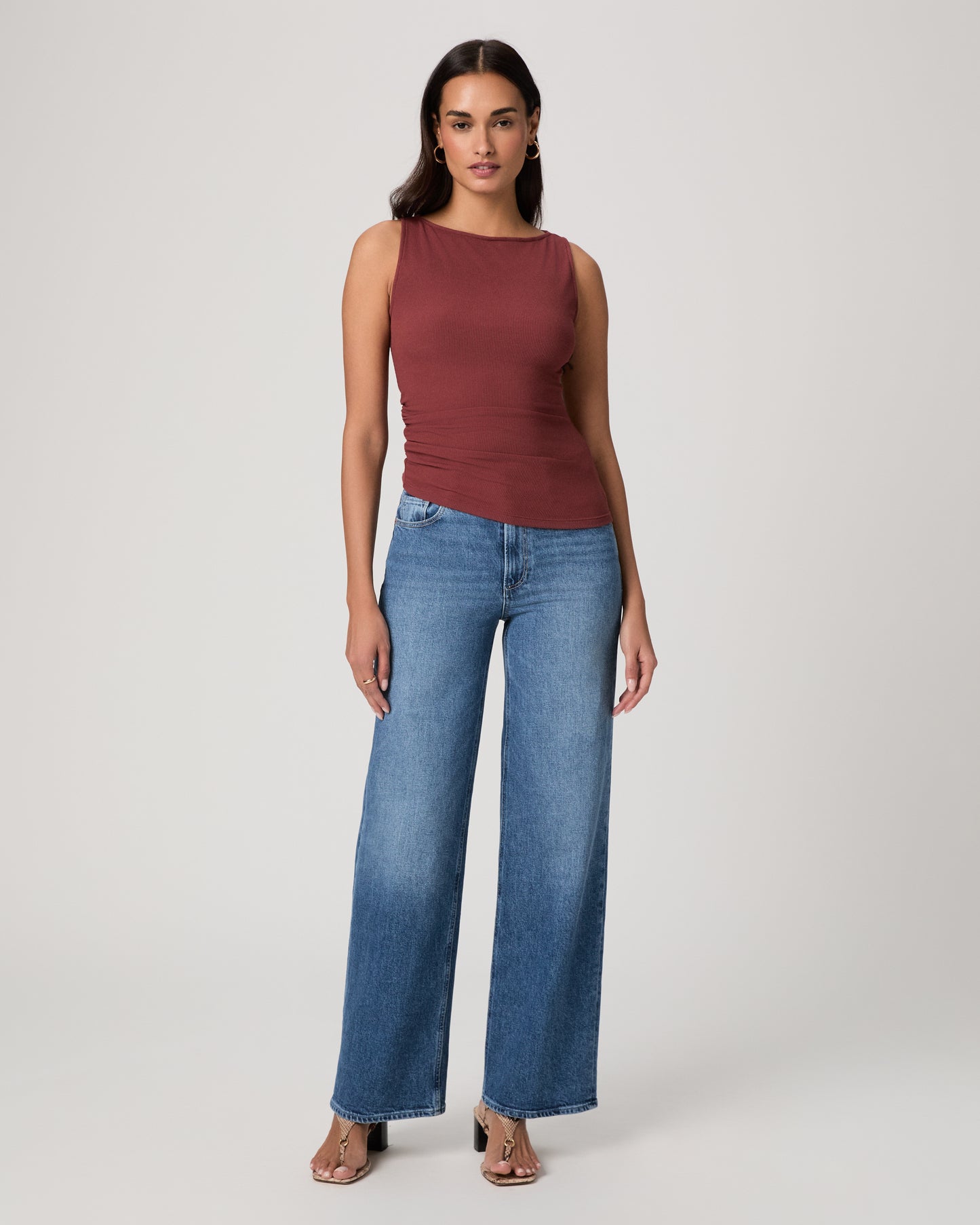 Woman wearing a burgundy sleeveless top and blue jeans on a white background