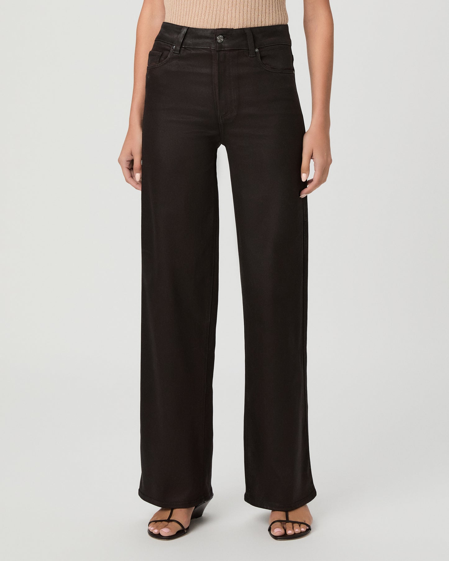 A woman modeling a pair of dark burgundy pants with cream color top and brown sandals against a light gray studio background.