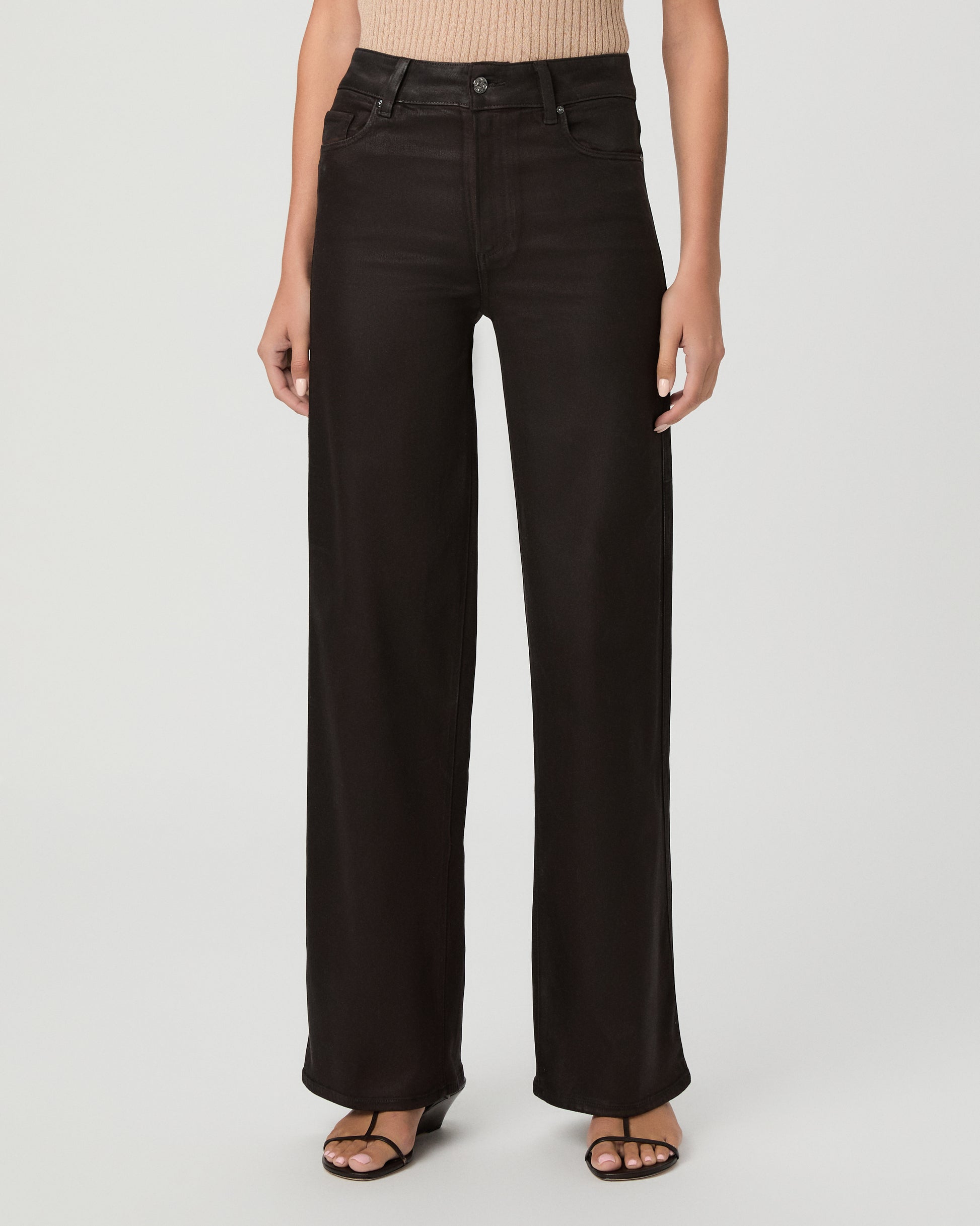 A woman modeling a pair of dark burgundy pants with cream color top and brown sandals against a light gray studio background.