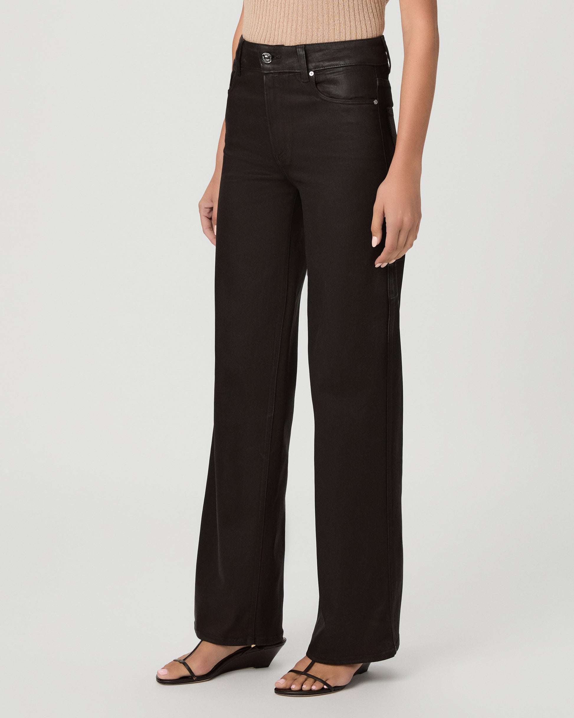 A woman modeling a pair of dark burgundy pants with cream color top and brown sandals against a light gray studio background.